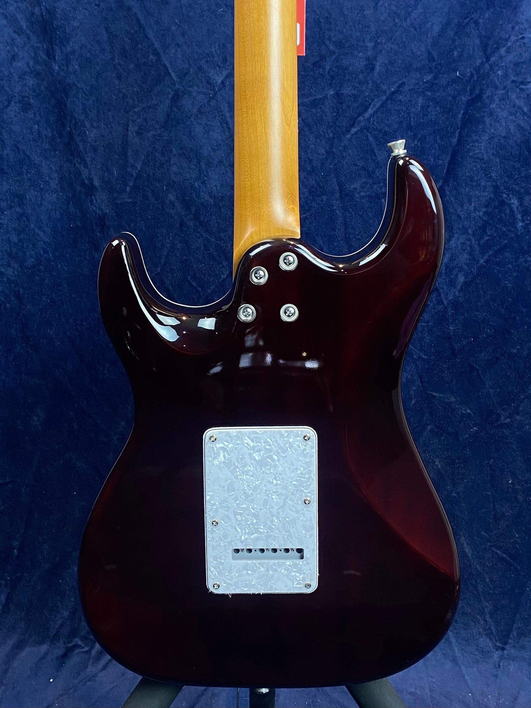 Rear view of an electric guitar with a dark glossy body, natural wood neck, and a rectangular white cover plate on the back.