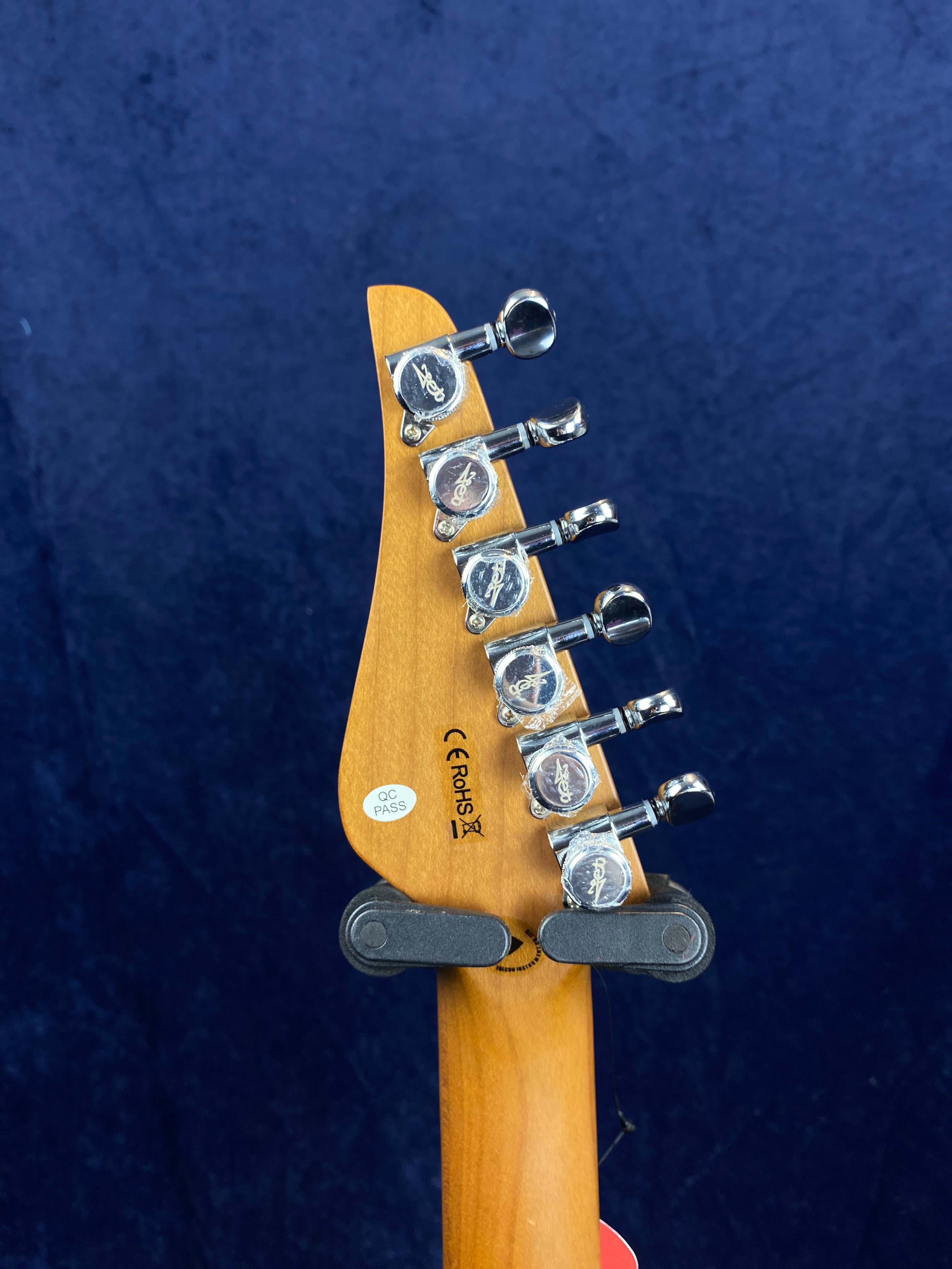 Back of electric guitar headstock showing six chrome tuning pegs, certification labels, and part of a wall hanger against a dark blue background.