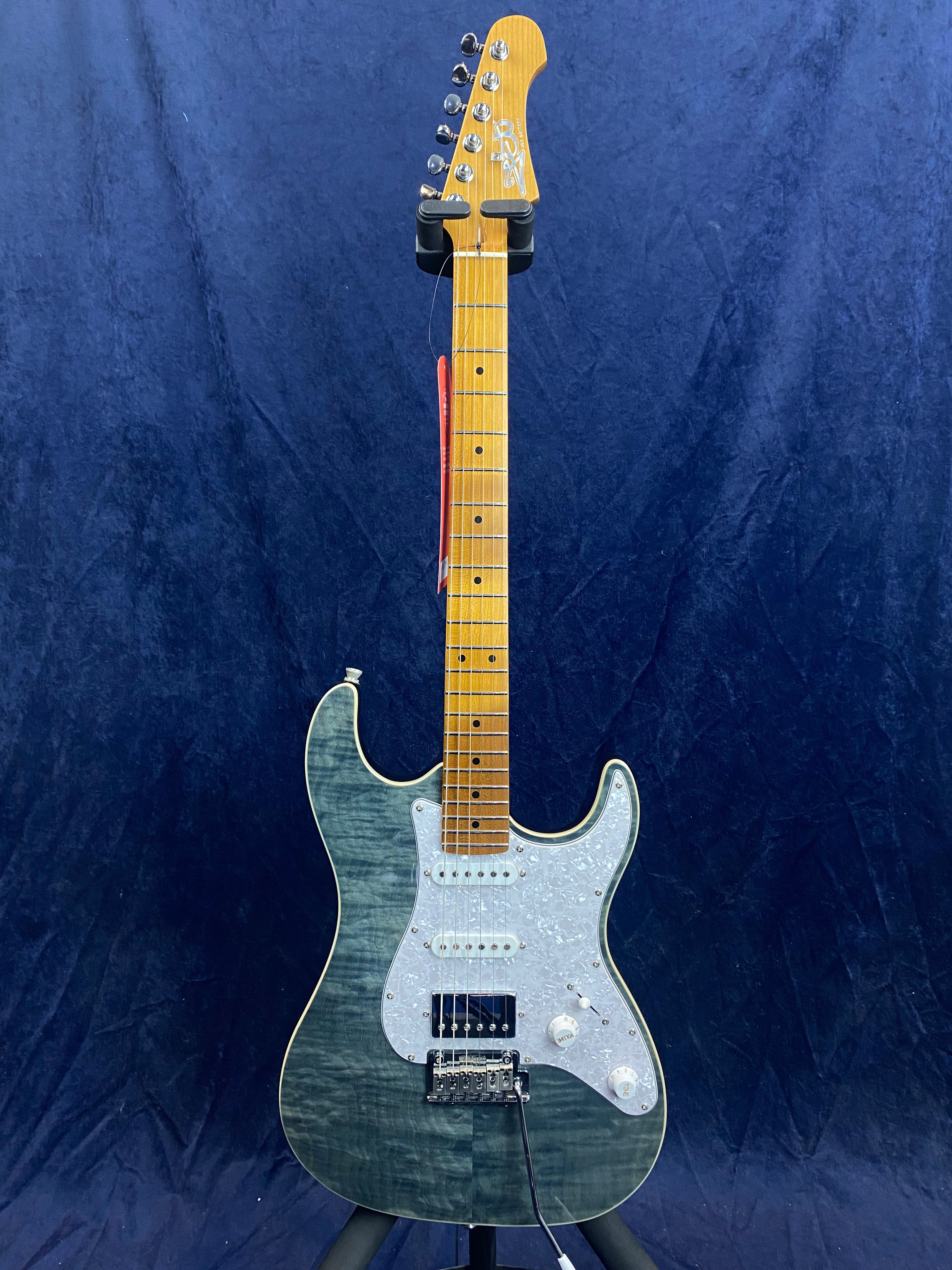 Electric guitar with a glossy blue-green quilted body, light wood neck, white pickguard, three pickups, and chrome hardware, standing upright on a stand.