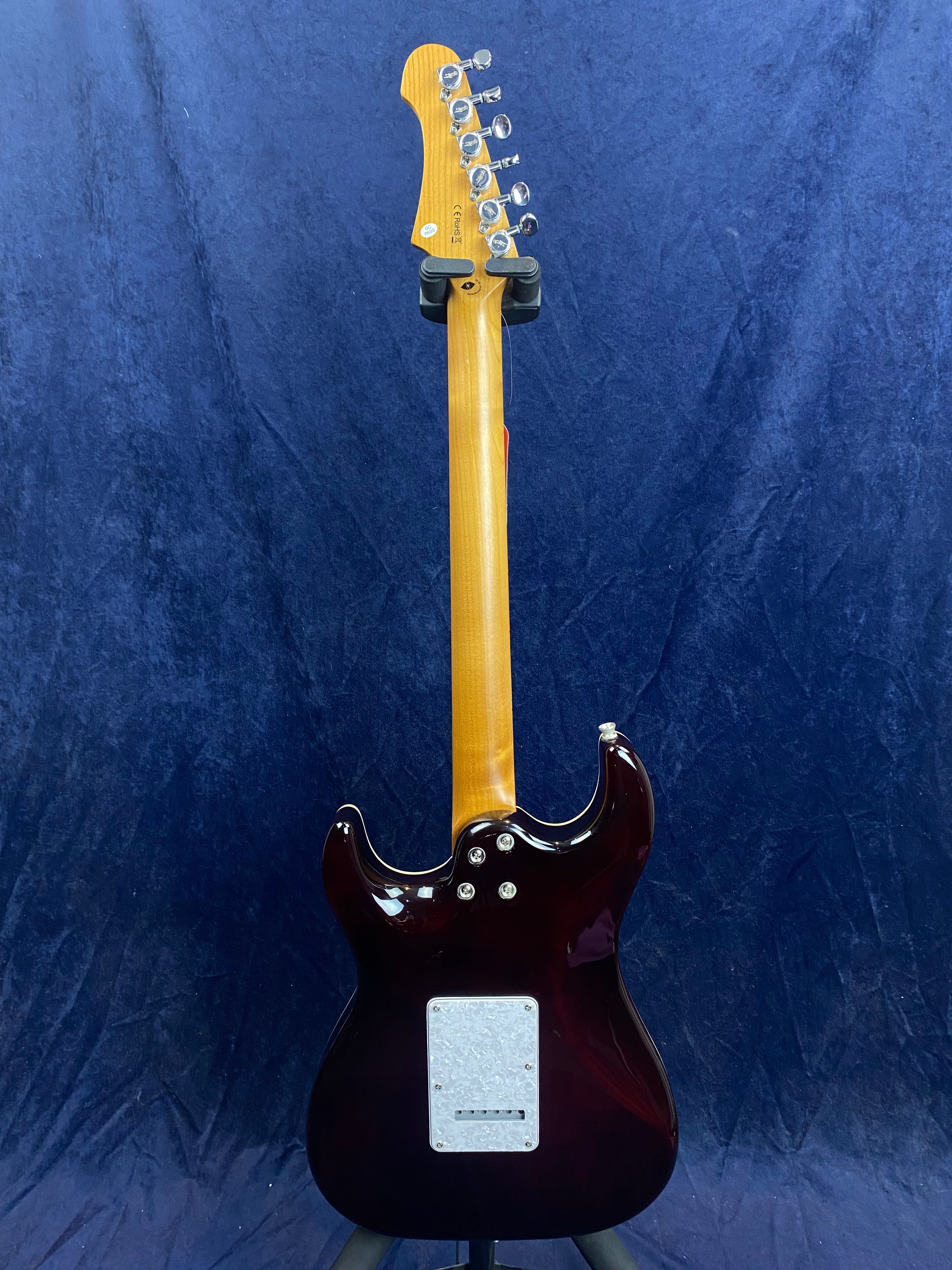 Electric guitar viewed from the back, showing a glossy dark brown body, light-colored neck, silver tuners, and a white plate near the base.