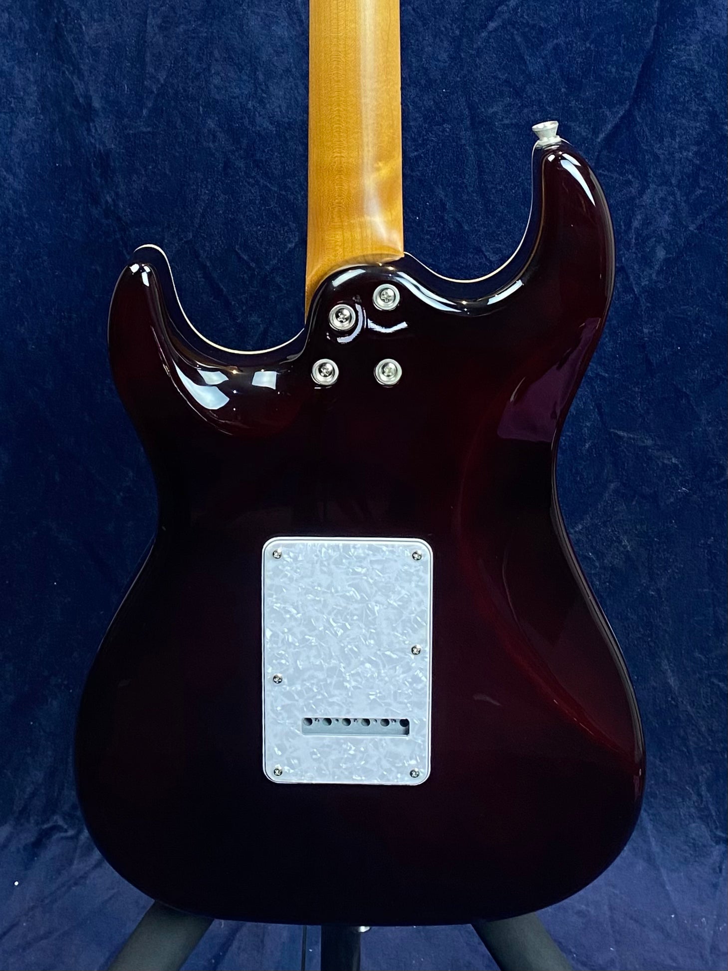 Rear view of a glossy dark reddish electric guitar body with a light-colored neck and a rectangular white backplate secured by screws.