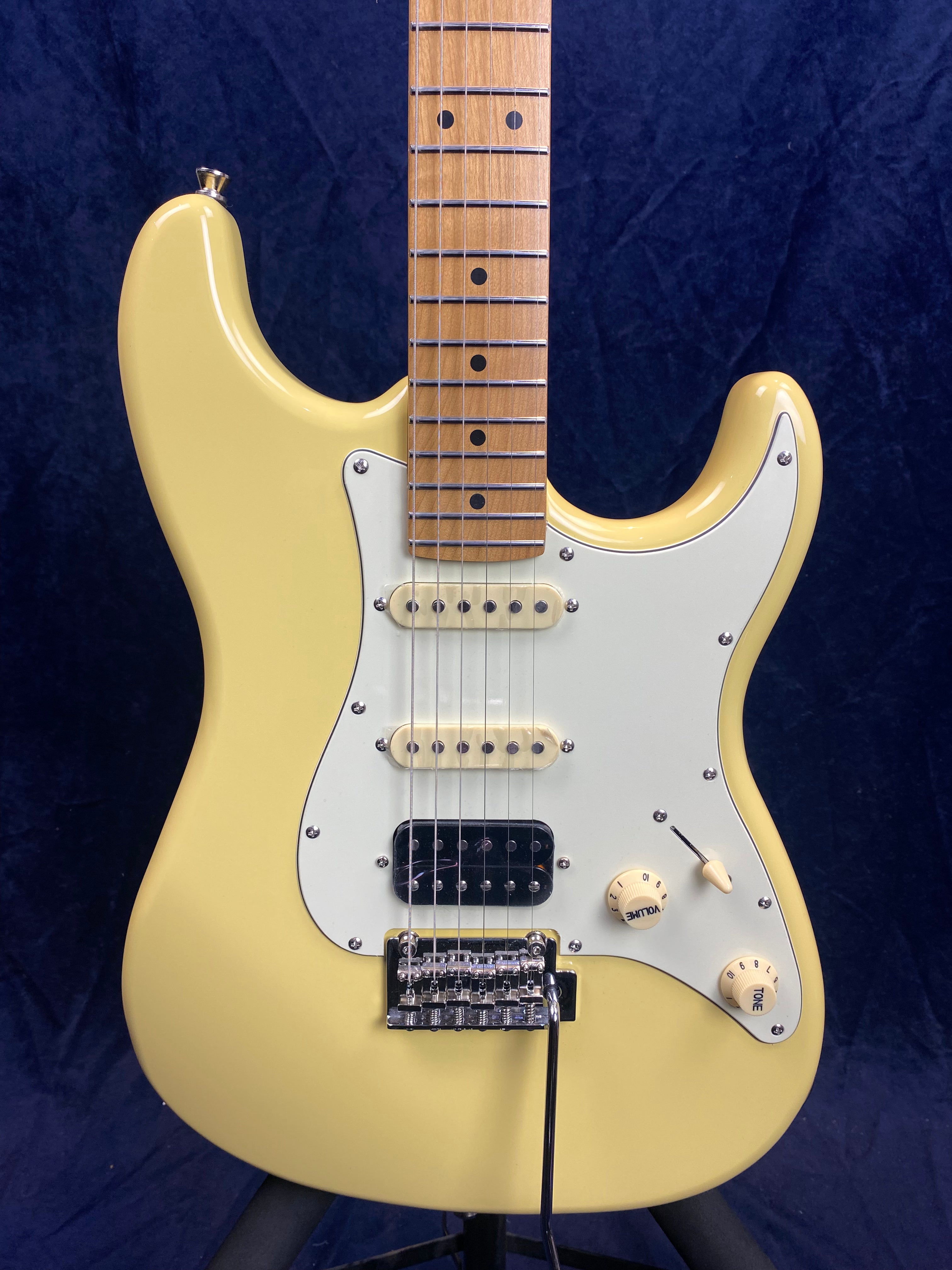 Yellow electric guitar with a white pickguard, three pickups, two control knobs, and a tremolo bridge against a dark blue background.