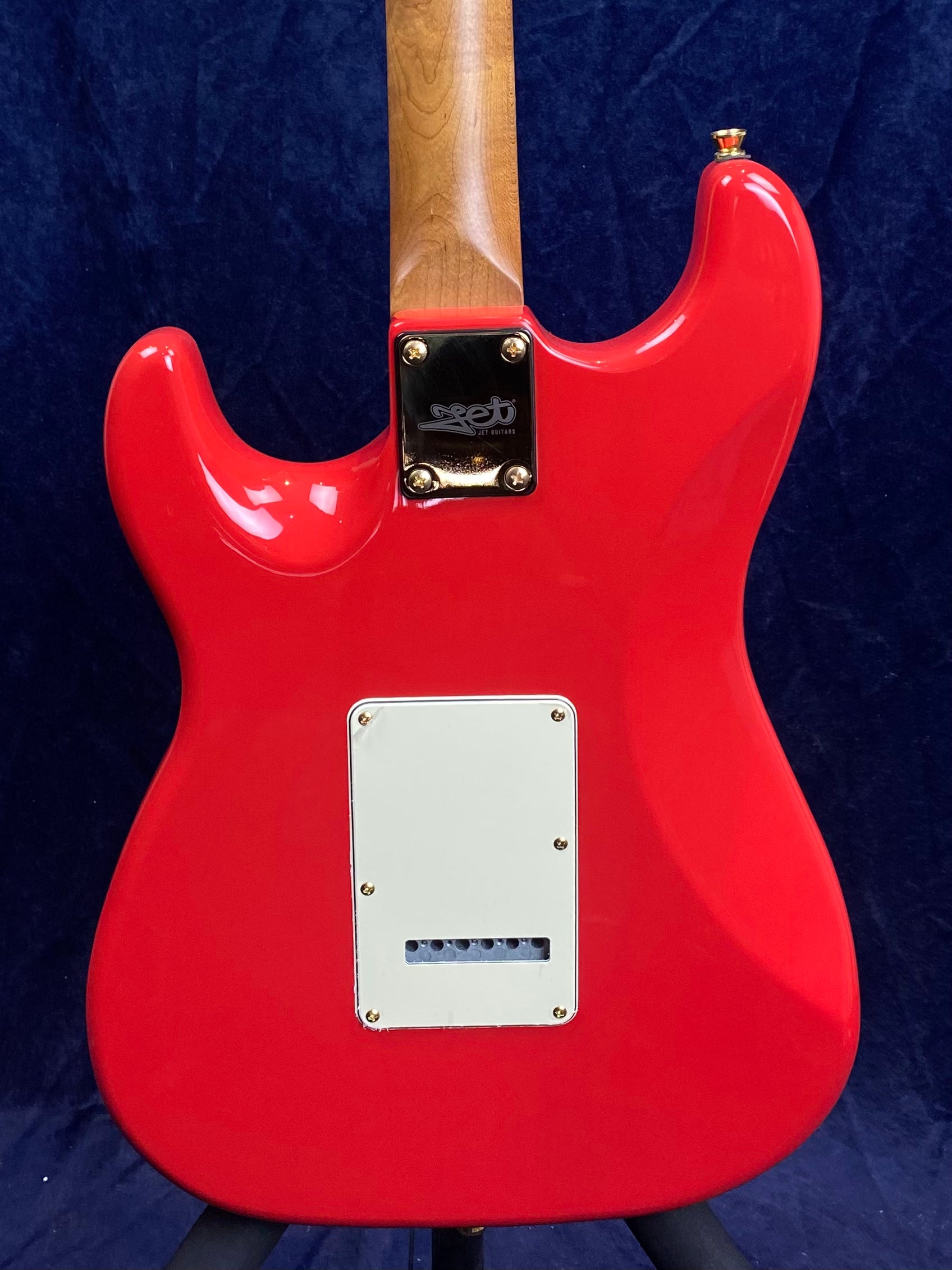 Bright red Jet electric guitar body shown from the back, white rectangular cover in the center, natural wood neck, gold neck plate with Jet logo.
