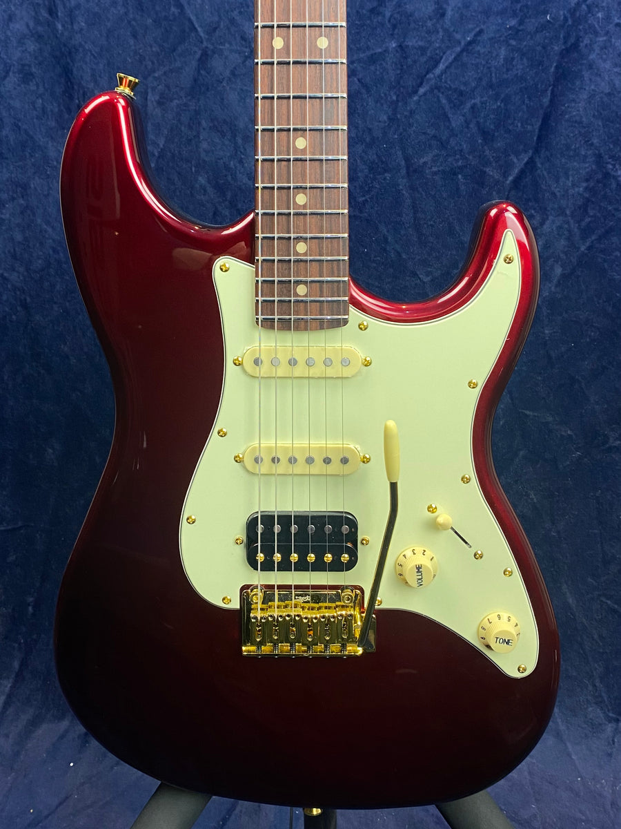 Metallic red electric guitar with a white pickguard, three pickups, gold hardware, and cream control knobs on a dark blue background.