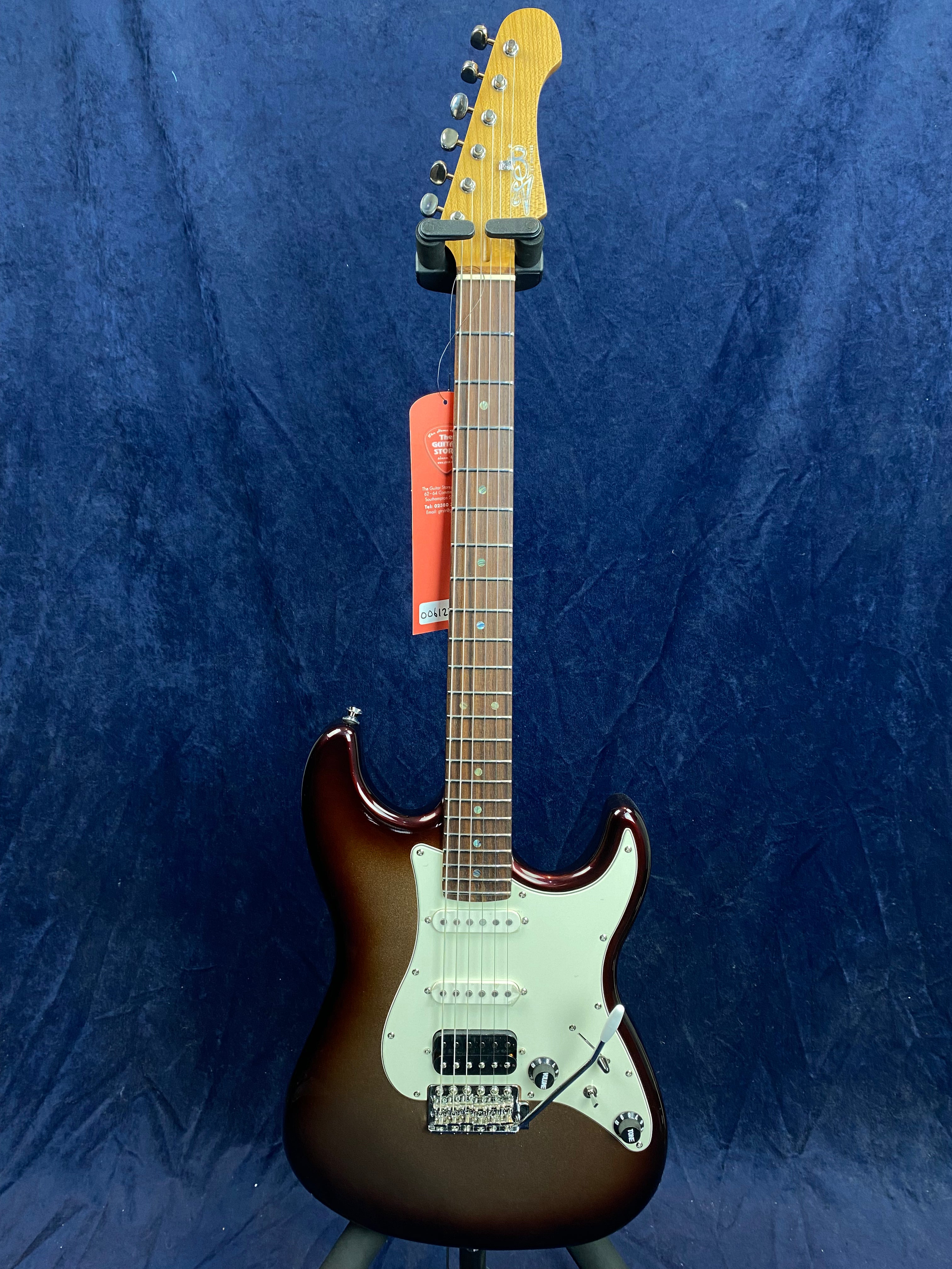 Sunburst electric guitar with a white pickguard, three pickups, maple neck, and chrome hardware, standing upright against a dark blue background.