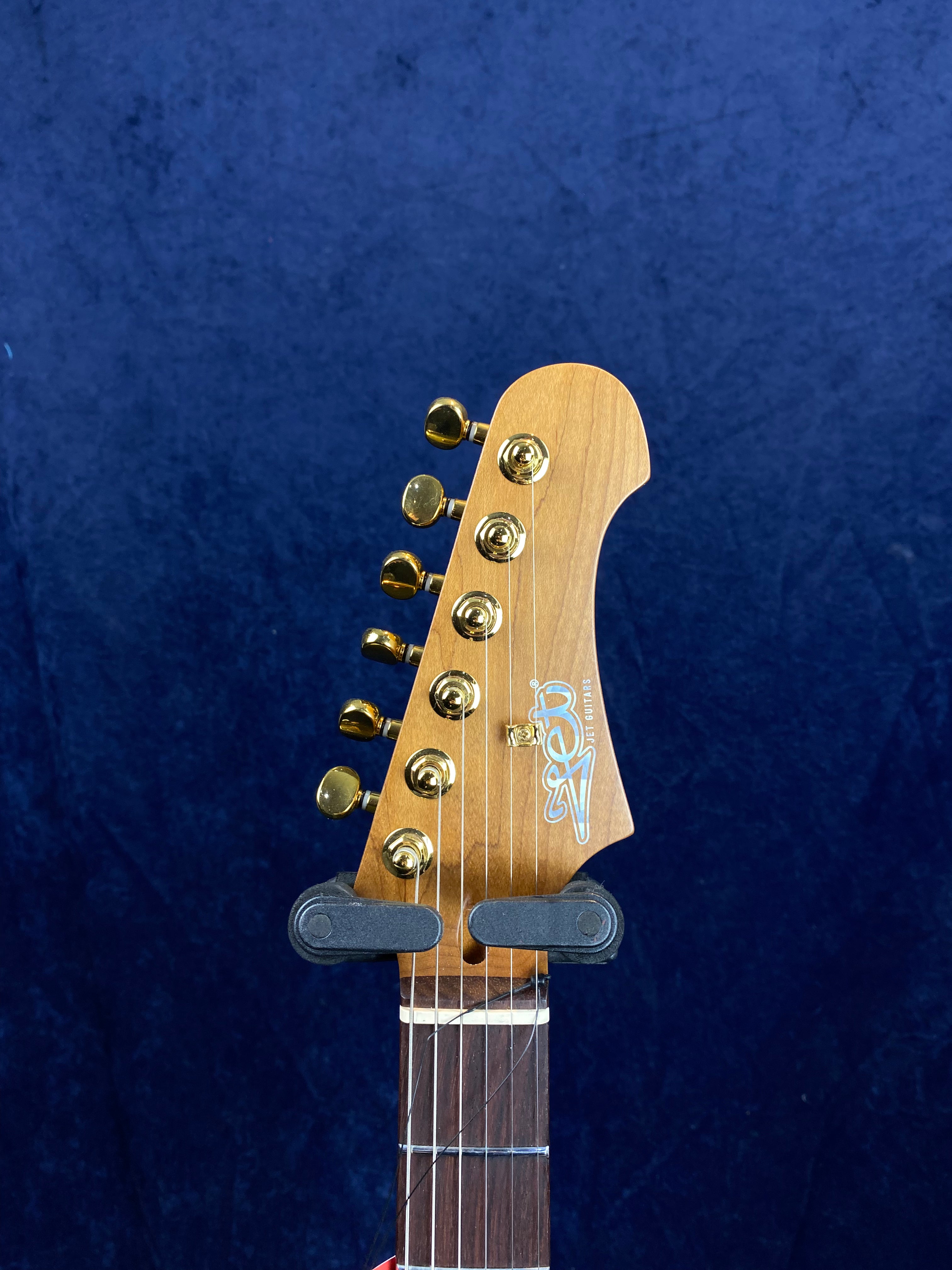 Electric guitar headstock with six gold tuning pegs, a wooden finish, and a logo that reads "Zeni ST5 GUITAR" against a dark blue background.