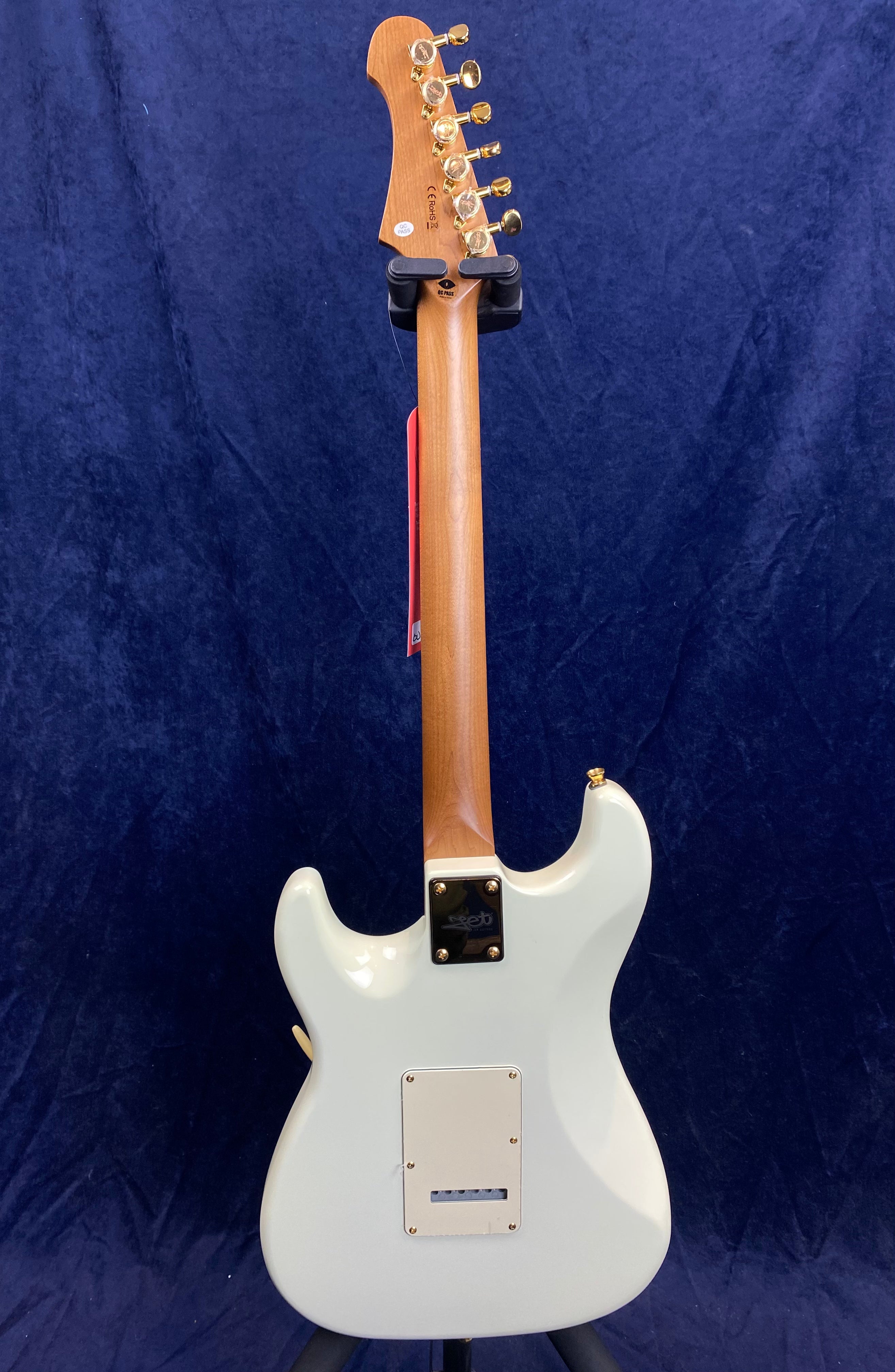 Electric guitar shown from the back, with a natural wood neck, white body, gold tuning pegs, and a square back plate near the bottom.