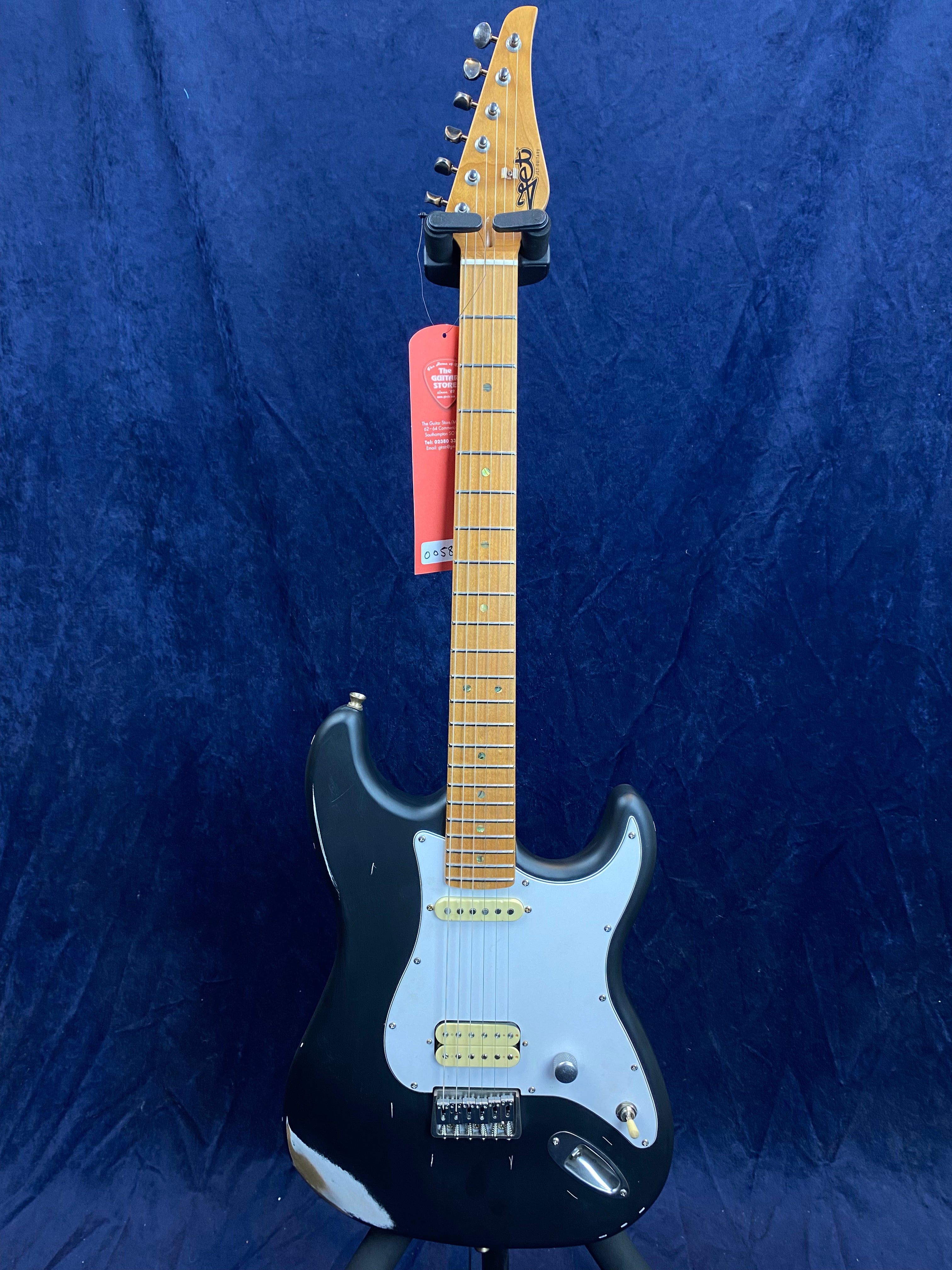 Black electric guitar with a maple neck, white pickguard, two humbucker pickups, and visible wear near the bottom edge.