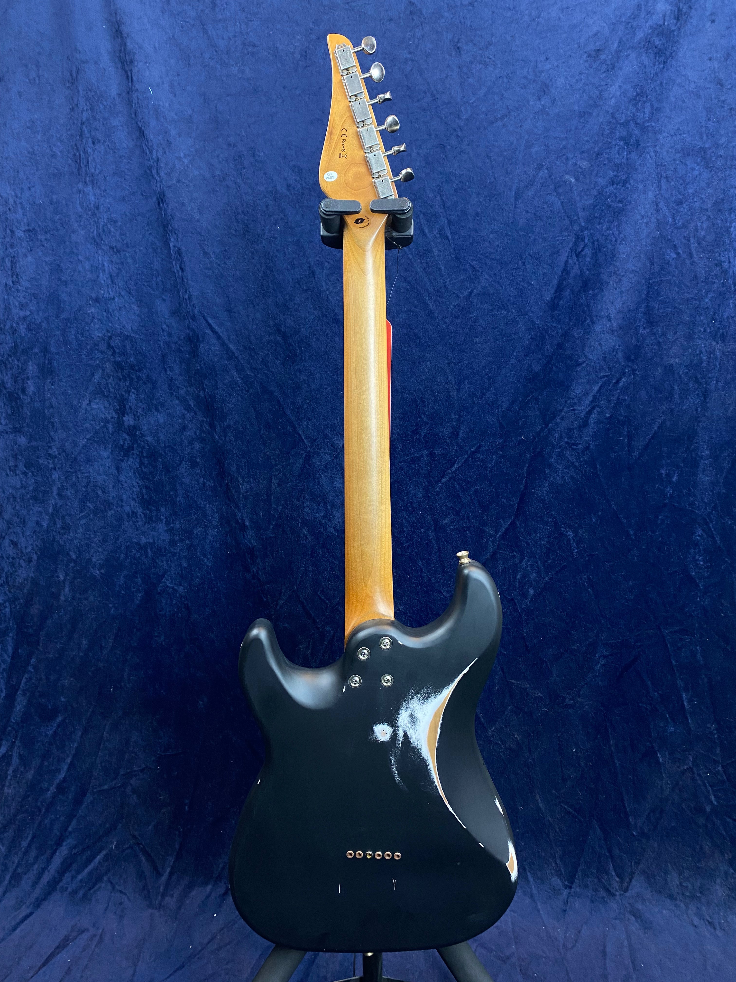Black electric guitar shown from the back, with a natural wood neck and visible paint wear on the rear body’s lower curve.