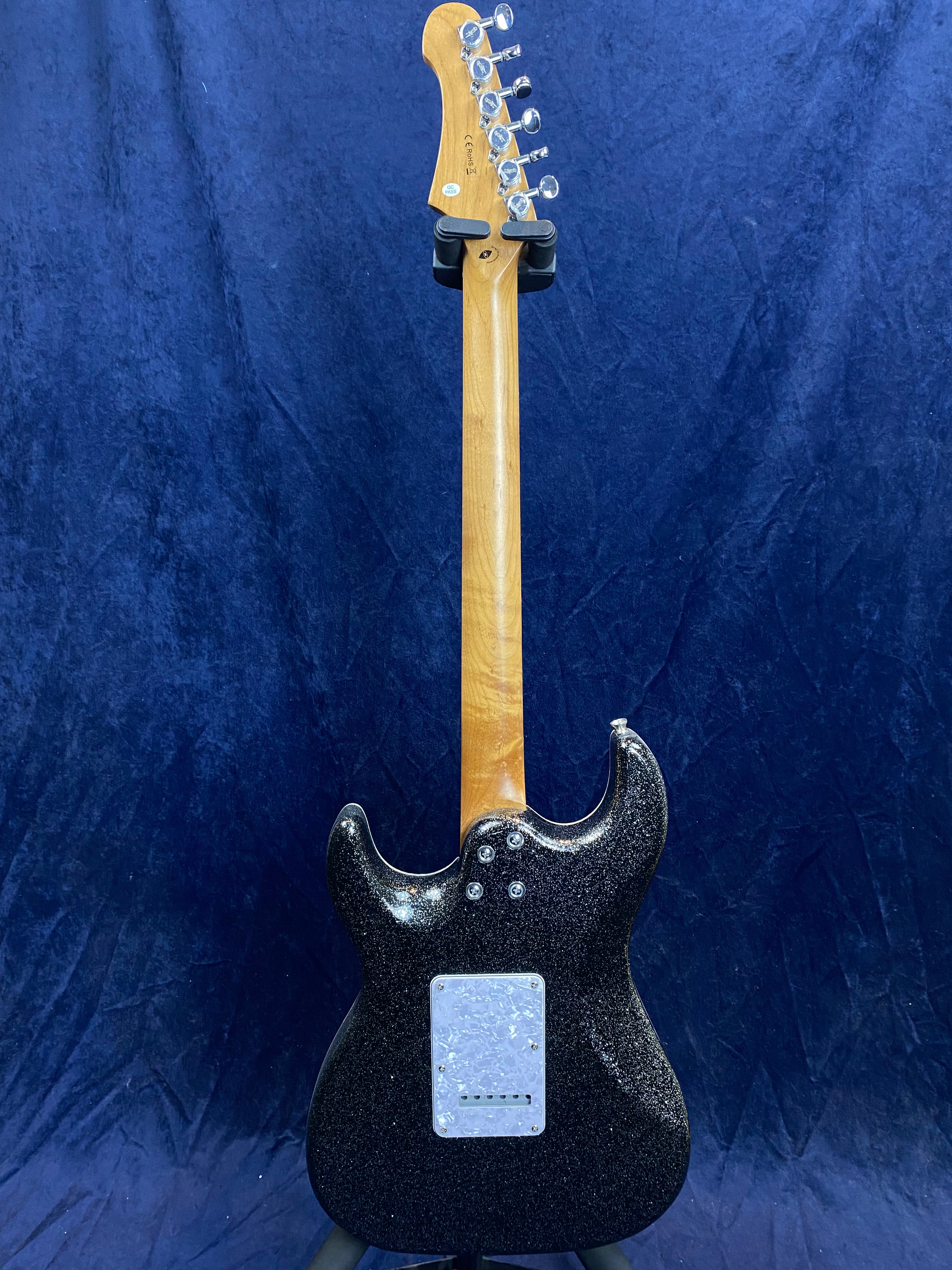 Electric guitar shown from the back with a glossy black body, light wood neck, six tuning pegs, and a white rectangular cover plate on the body.