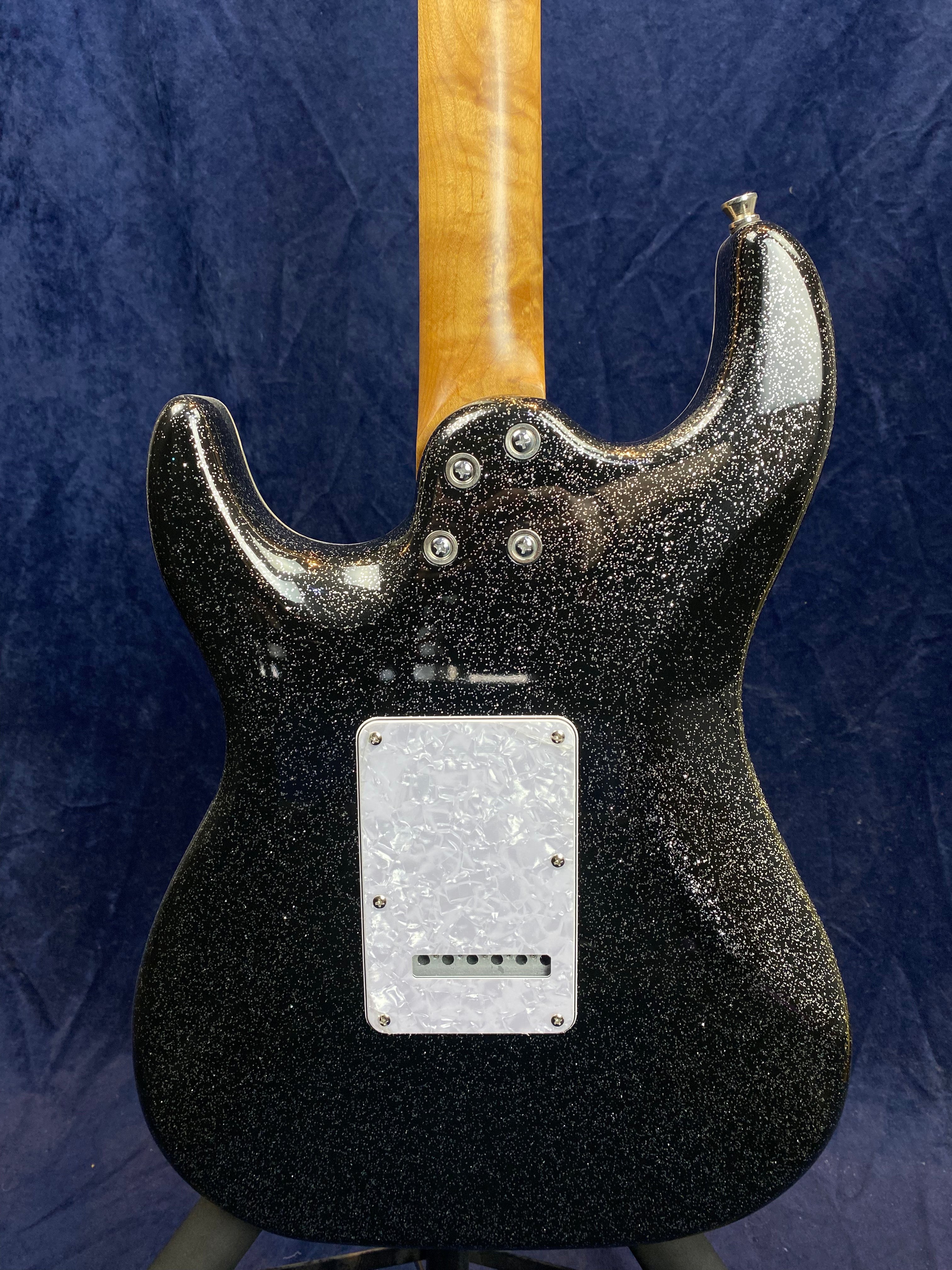 Black electric guitar with a sparkly finish, natural wood neck, and a white pearloid backplate covering the tremolo cavity.