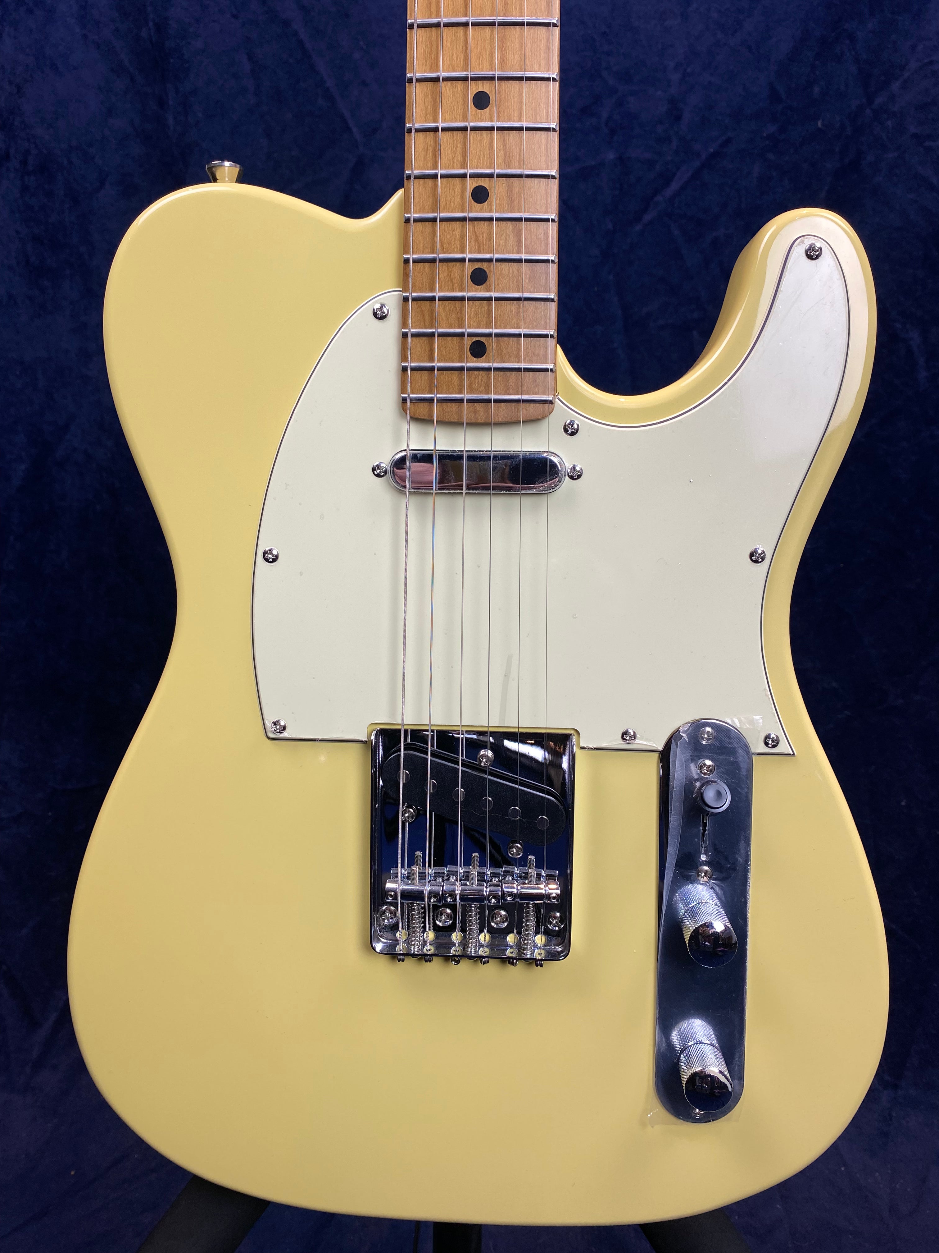 Cream-colored electric guitar with a white pickguard, chrome bridge, two chrome knobs, and a maple neck with dot inlays.