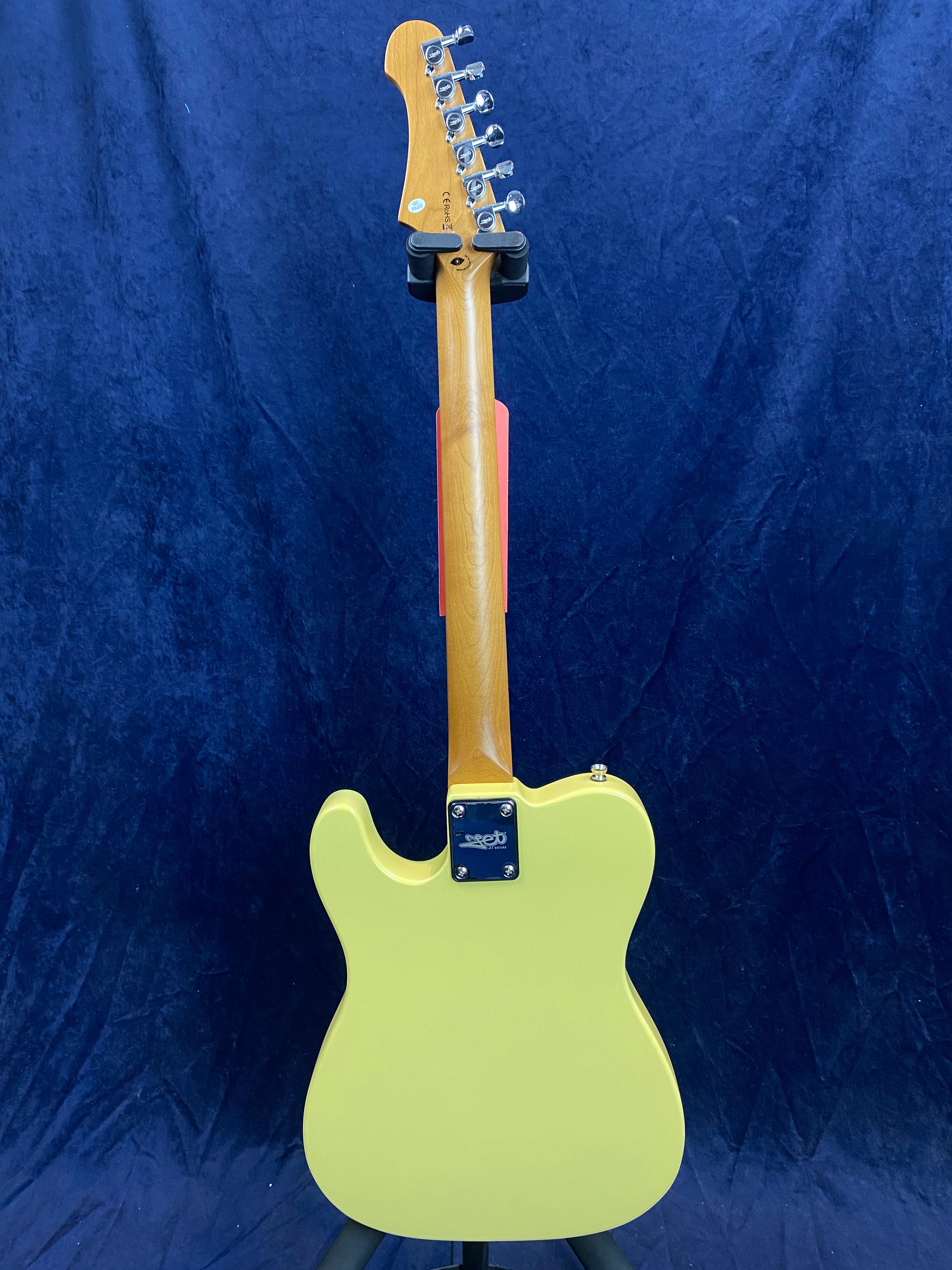 Yellow electric guitar shown from the back, with a maple neck, chrome tuners, and a rectangular neck plate. Blue backdrop.