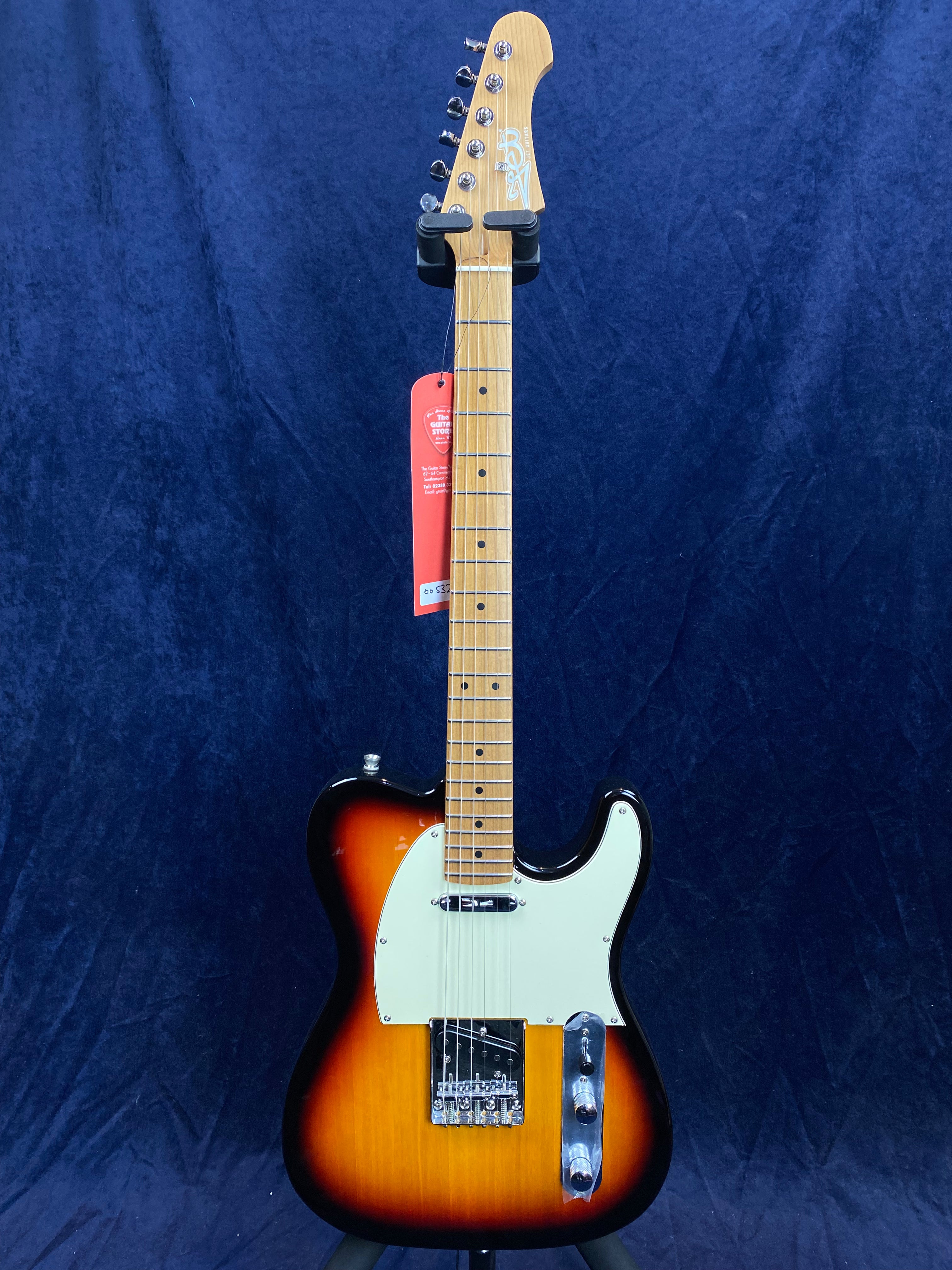 Sunburst-finish electric guitar with white pickguard, maple neck and fingerboard, six tuning pegs, and a red tag hanging from the headstock.