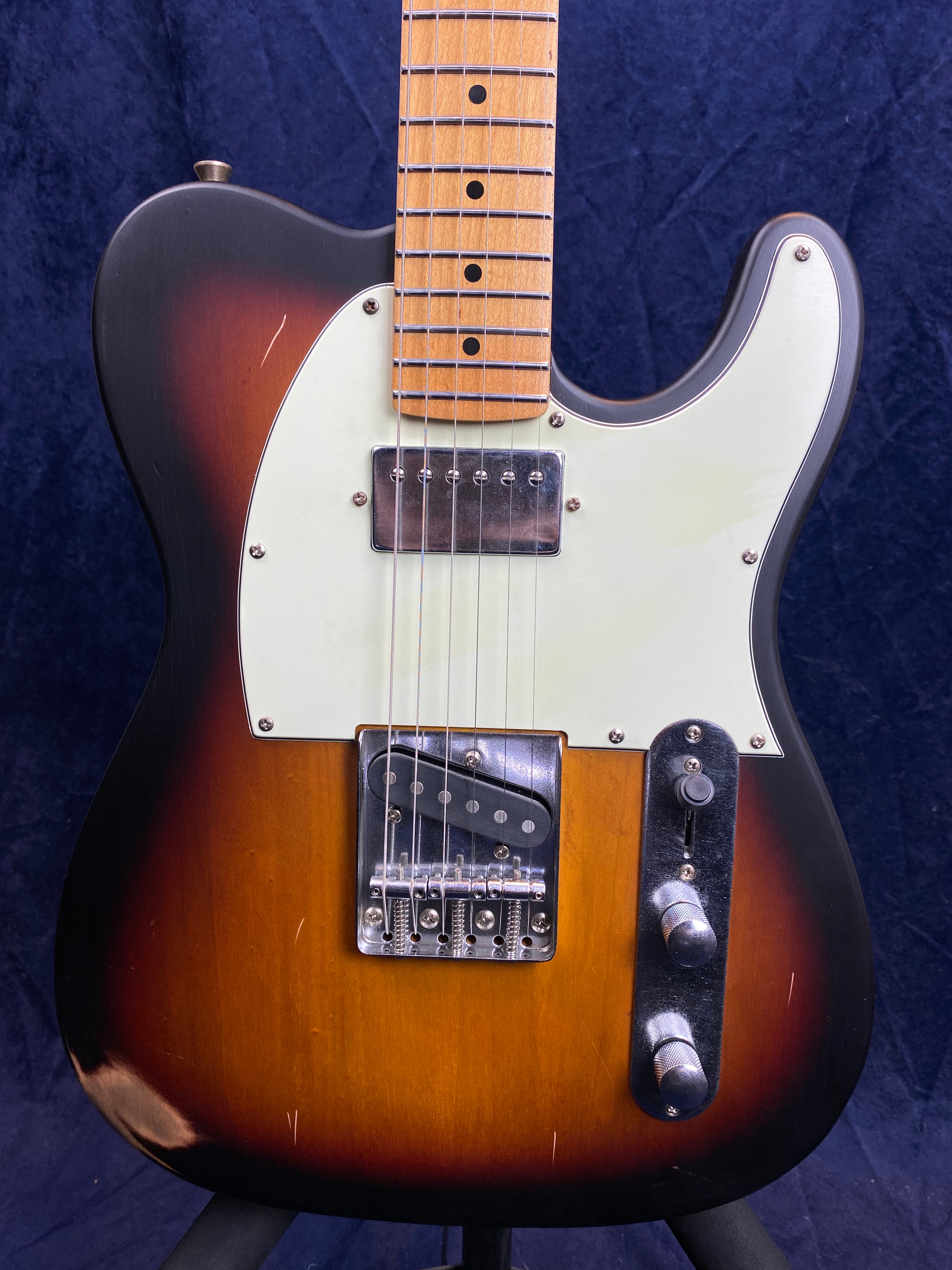 Electric guitar with a sunburst finish, white pickguard, two pickups, chrome bridge, and two control knobs on a metal plate. Some visible scratches.