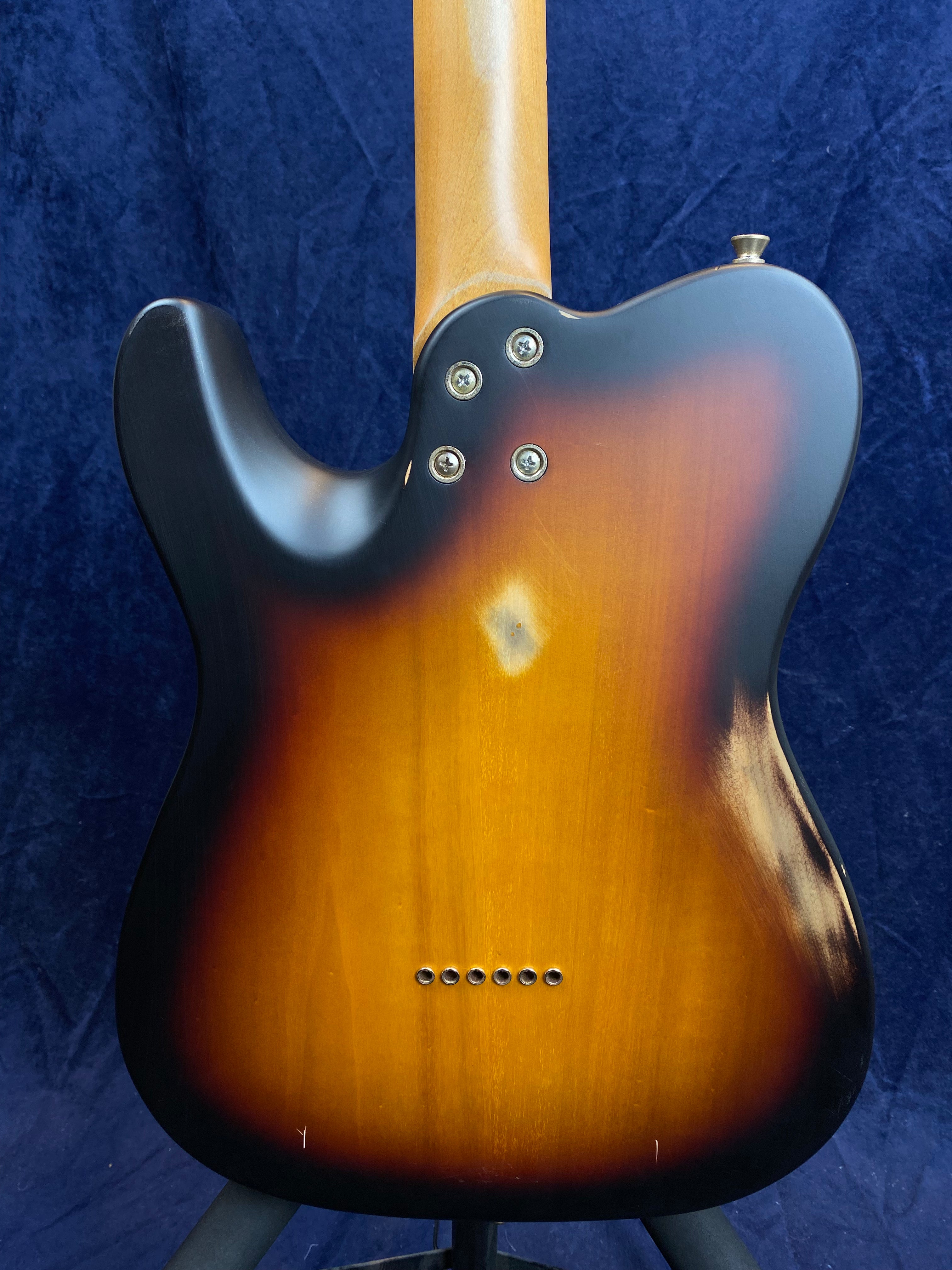 Back of a sunburst electric guitar showing four neck bolts, slight wear marks, and six string holes along the bottom.