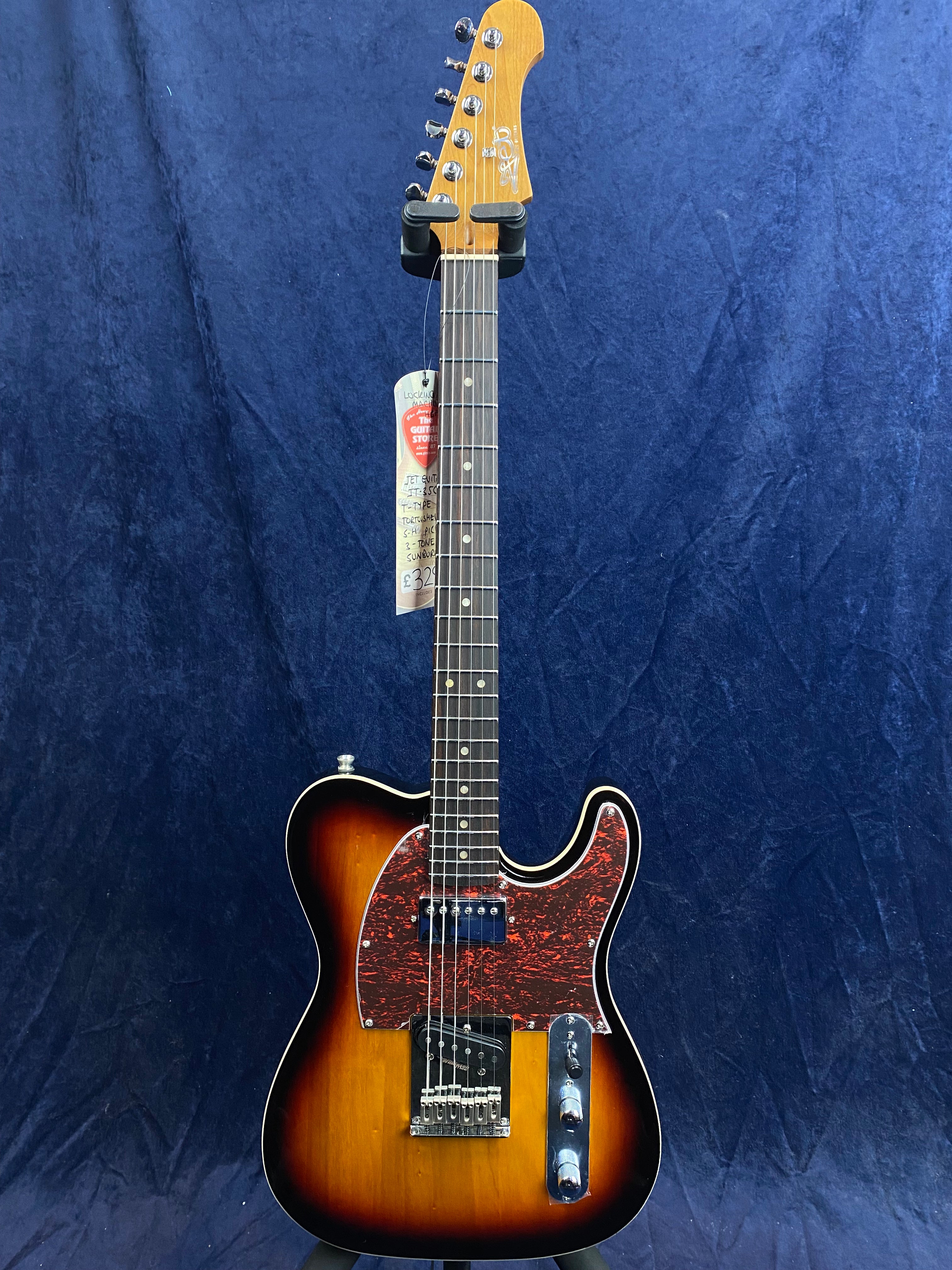 Sunburst electric guitar with a red tortoiseshell pickguard, two pickups, chrome controls, and a maple neck, displayed against a dark blue background.