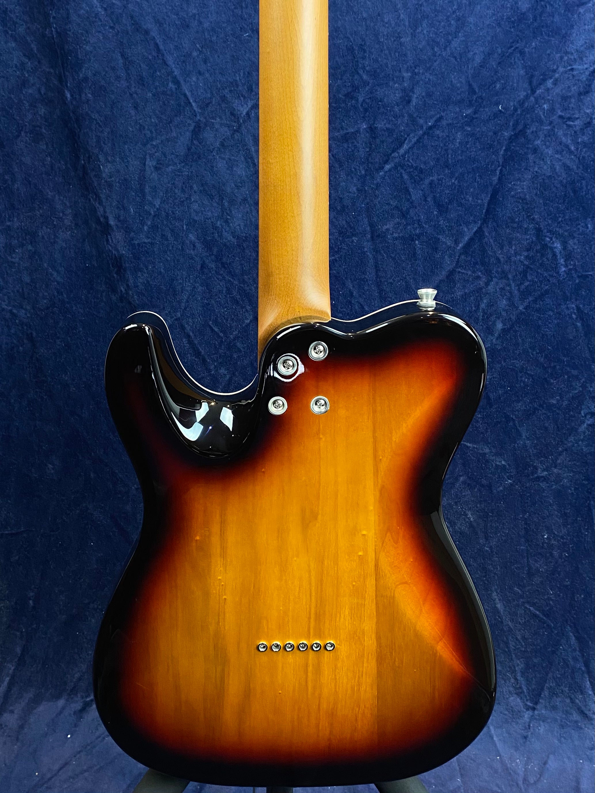 Electric guitar rear view with a sunburst finish, six bridge string ferrules, two neck bolts, and a natural wood neck against a dark background.