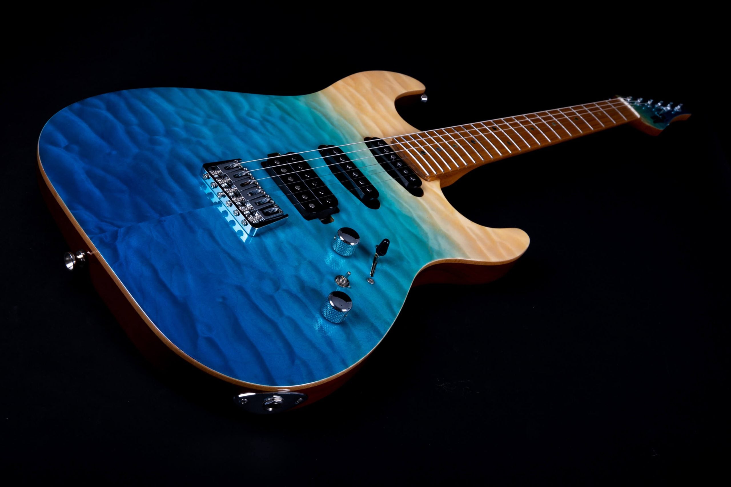 Electric guitar with a quilted finish, blue fading to natural wood, three black pickups, chrome hardware, and two control knobs.