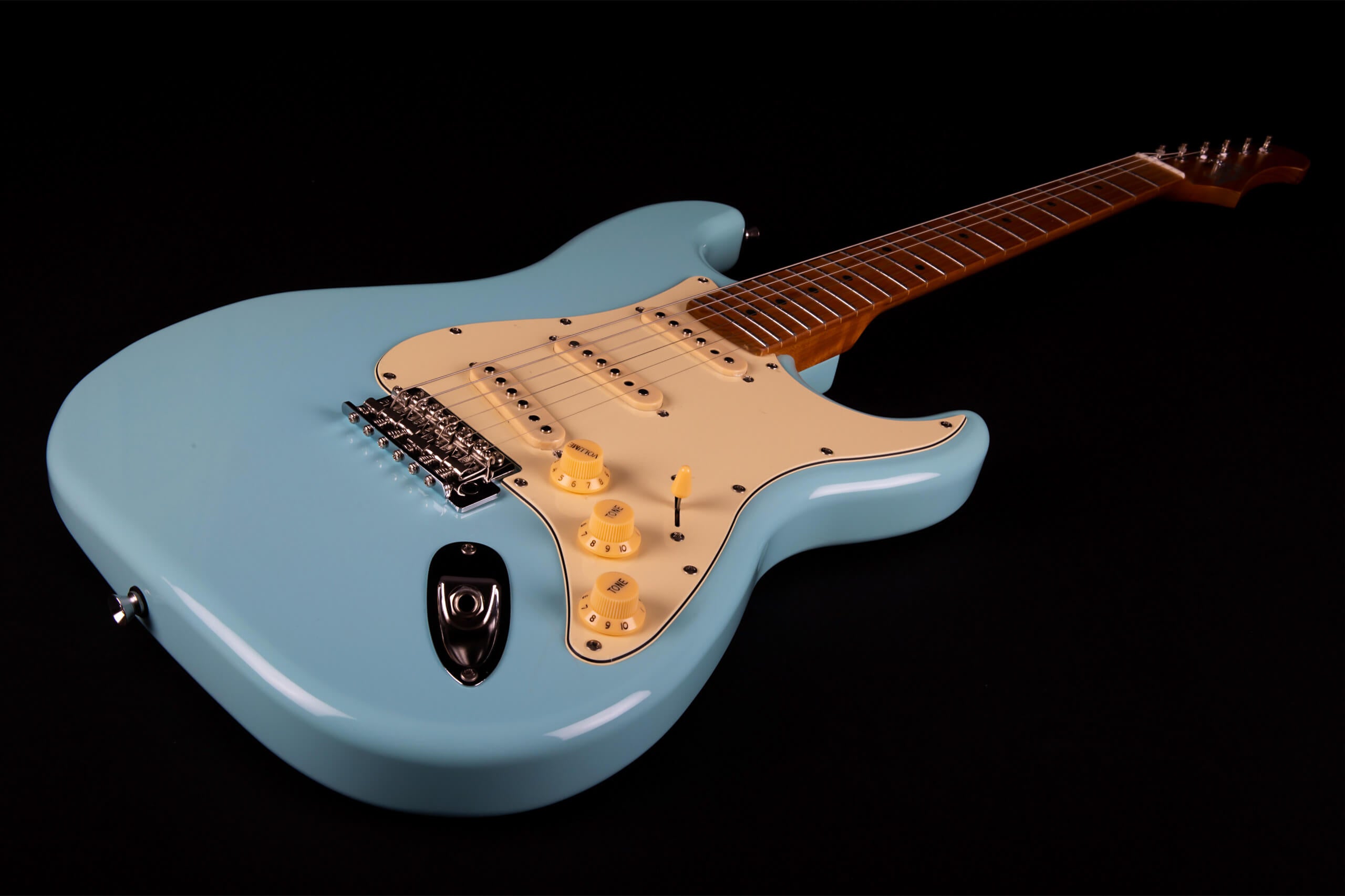 Light blue electric guitar with a cream pickguard, three single-coil pickups, three control knobs, and a brown neck with silver frets and tuning pegs.