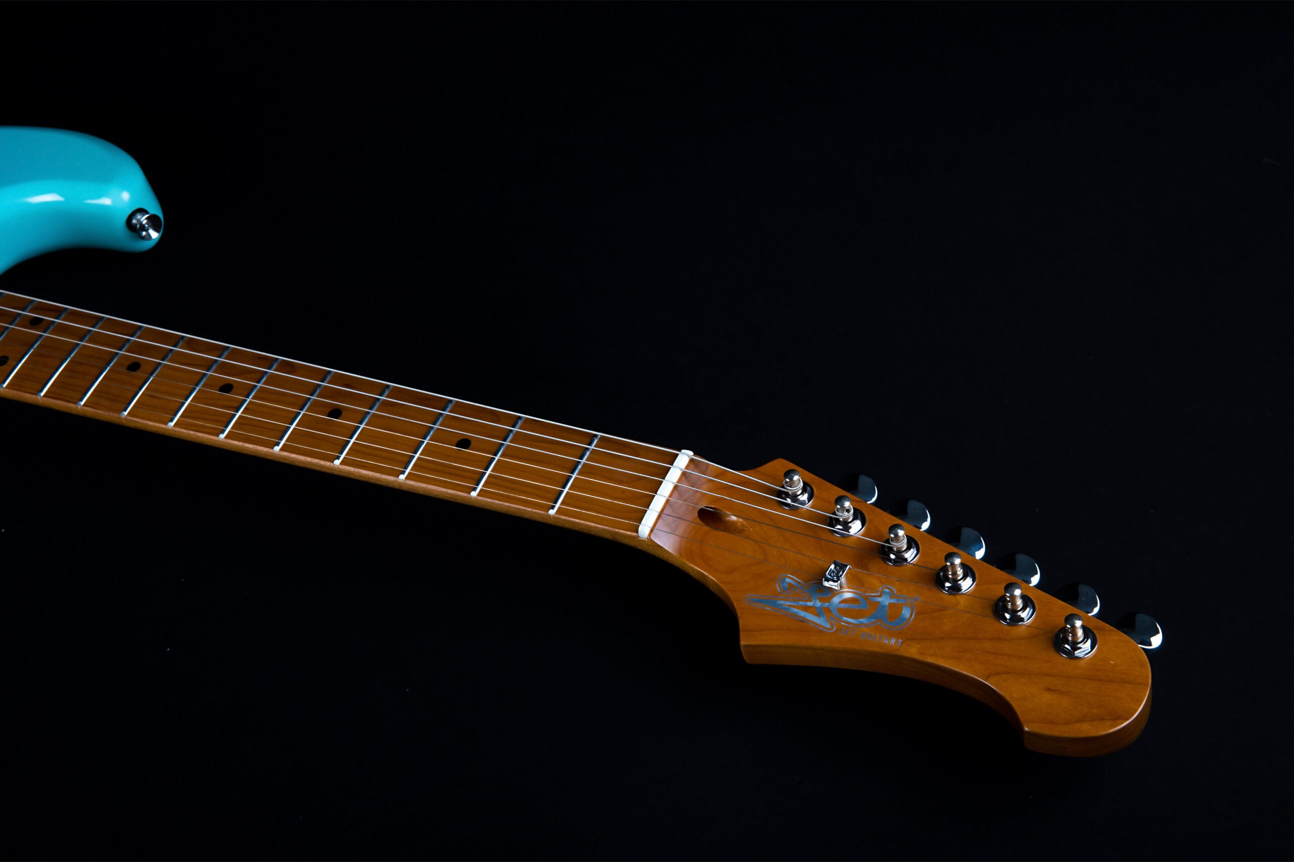 Light blue electric guitar showing the neck and headstock with six tuning pegs, dot inlays, and Zet logo on a dark background.