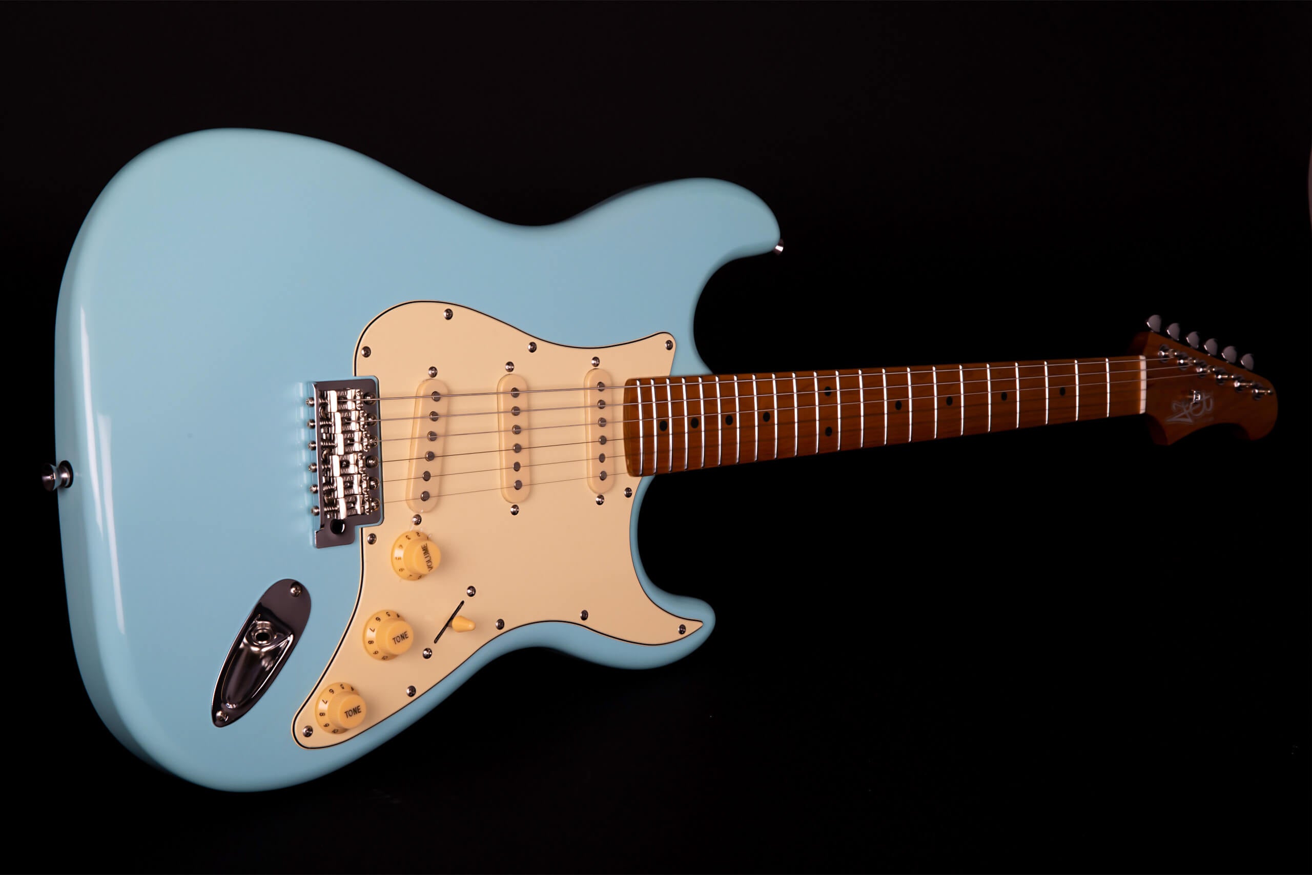Light blue electric guitar with cream pickguard, three single-coil pickups, yellow knobs, and a brown fretboard against a black background.