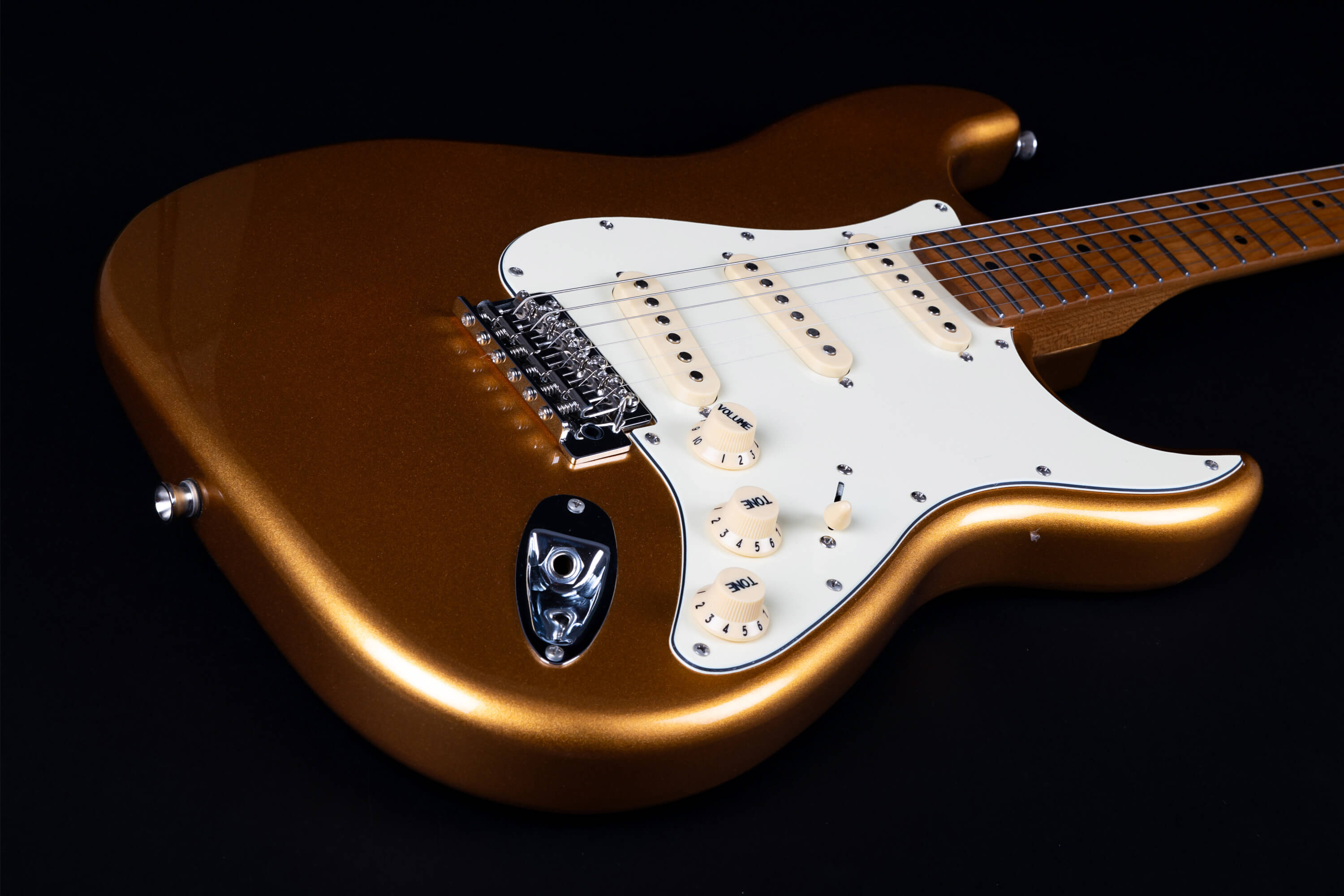 Metallic gold electric guitar with a white pickguard, three single-coil pickups, control knobs, and a maple fretboard.