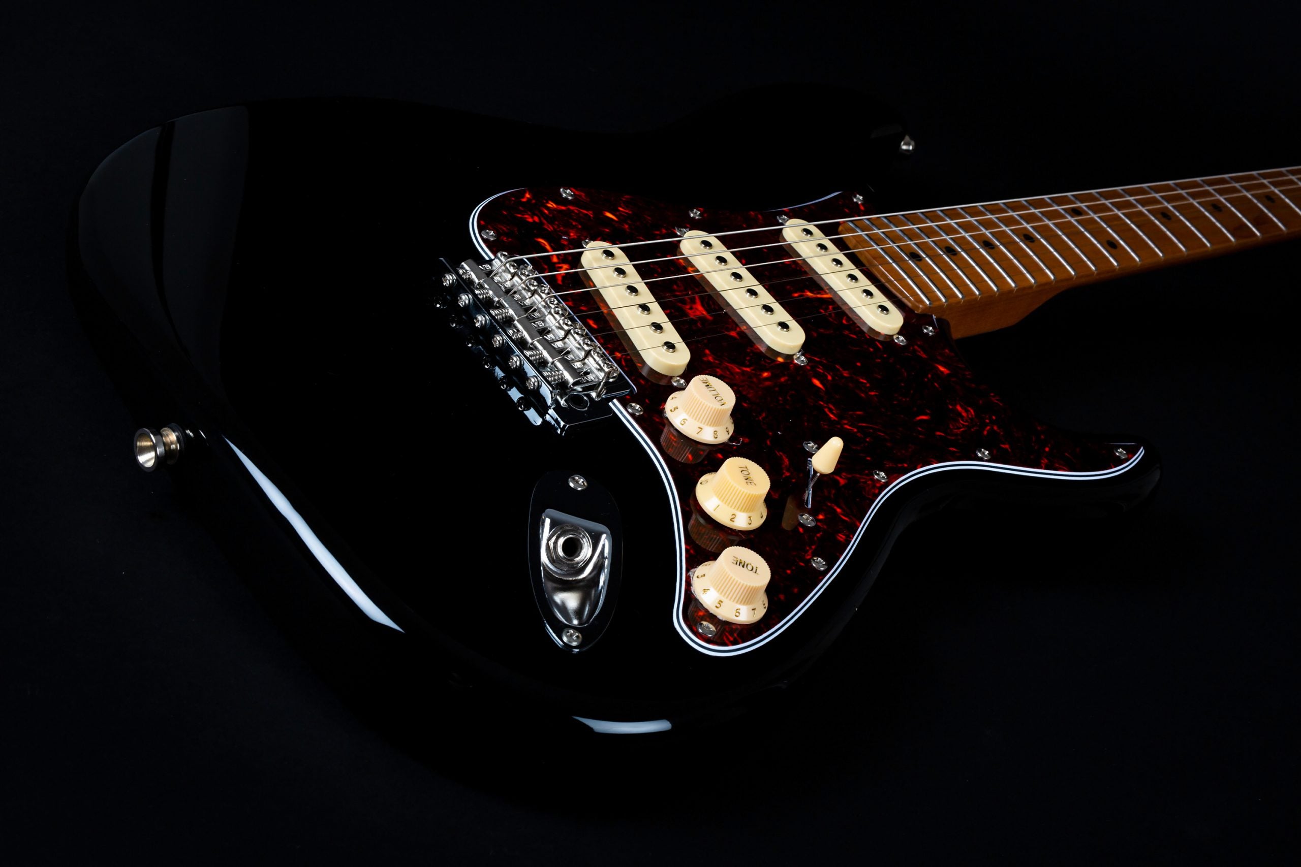 Glossy black electric guitar with a reddish tortoiseshell pickguard, three cream single-coil pickups, cream knobs, and a maple neck.