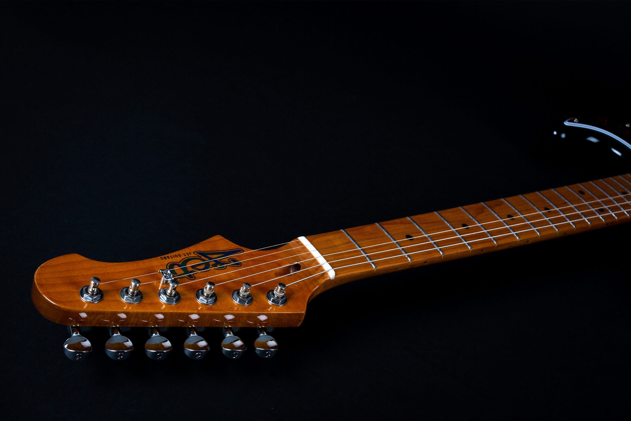 Electric guitar headstock and fretboard in natural wood finish, six tuning pegs, metal frets, and dot inlays on a black background.