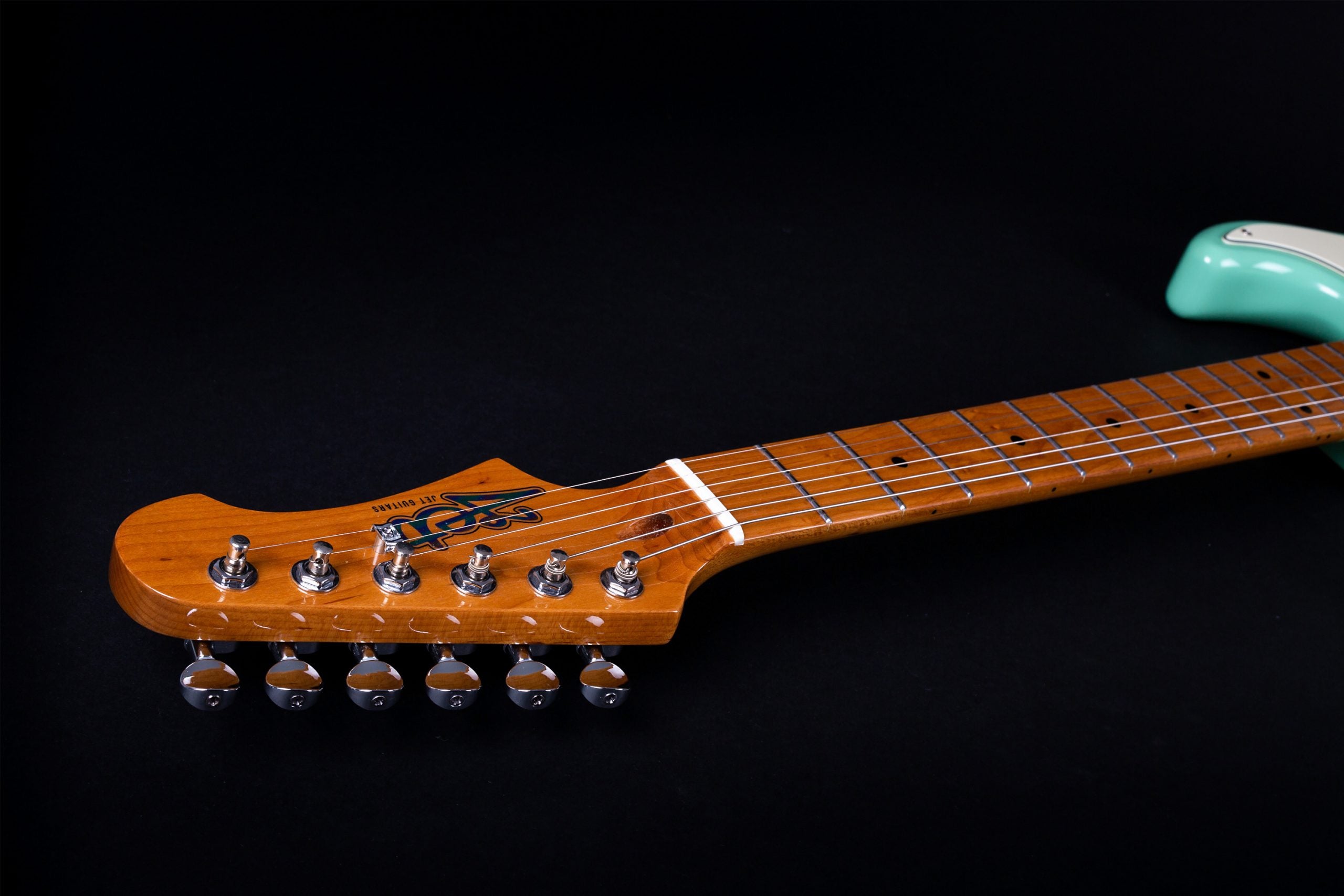 Light brown electric guitar neck and headstock with six silver tuning pegs, attached to a mint green body, viewed on a black background.