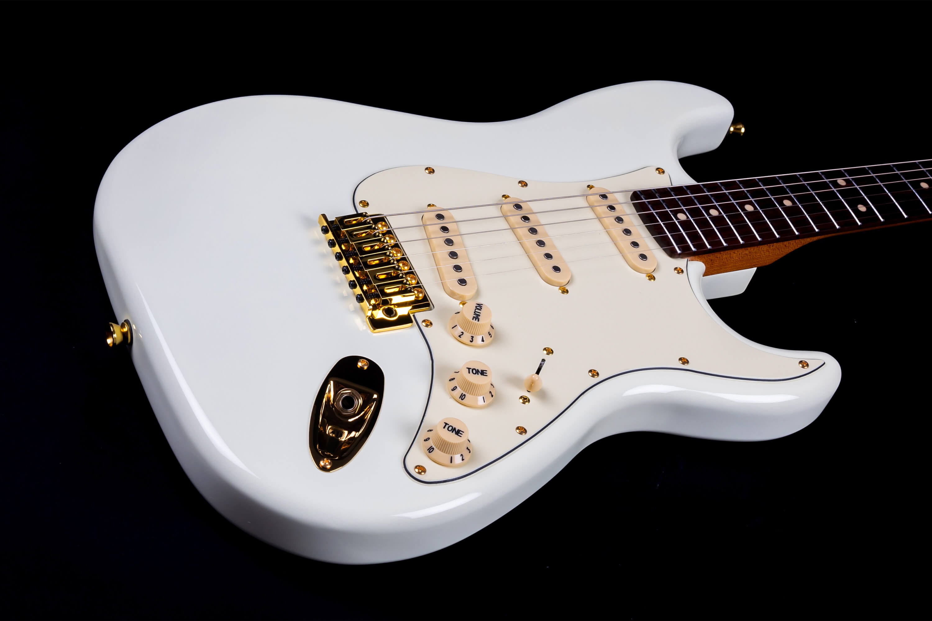 White electric guitar with gold hardware, three single-coil pickups, cream knobs, five-way switch, and a dark fingerboard.