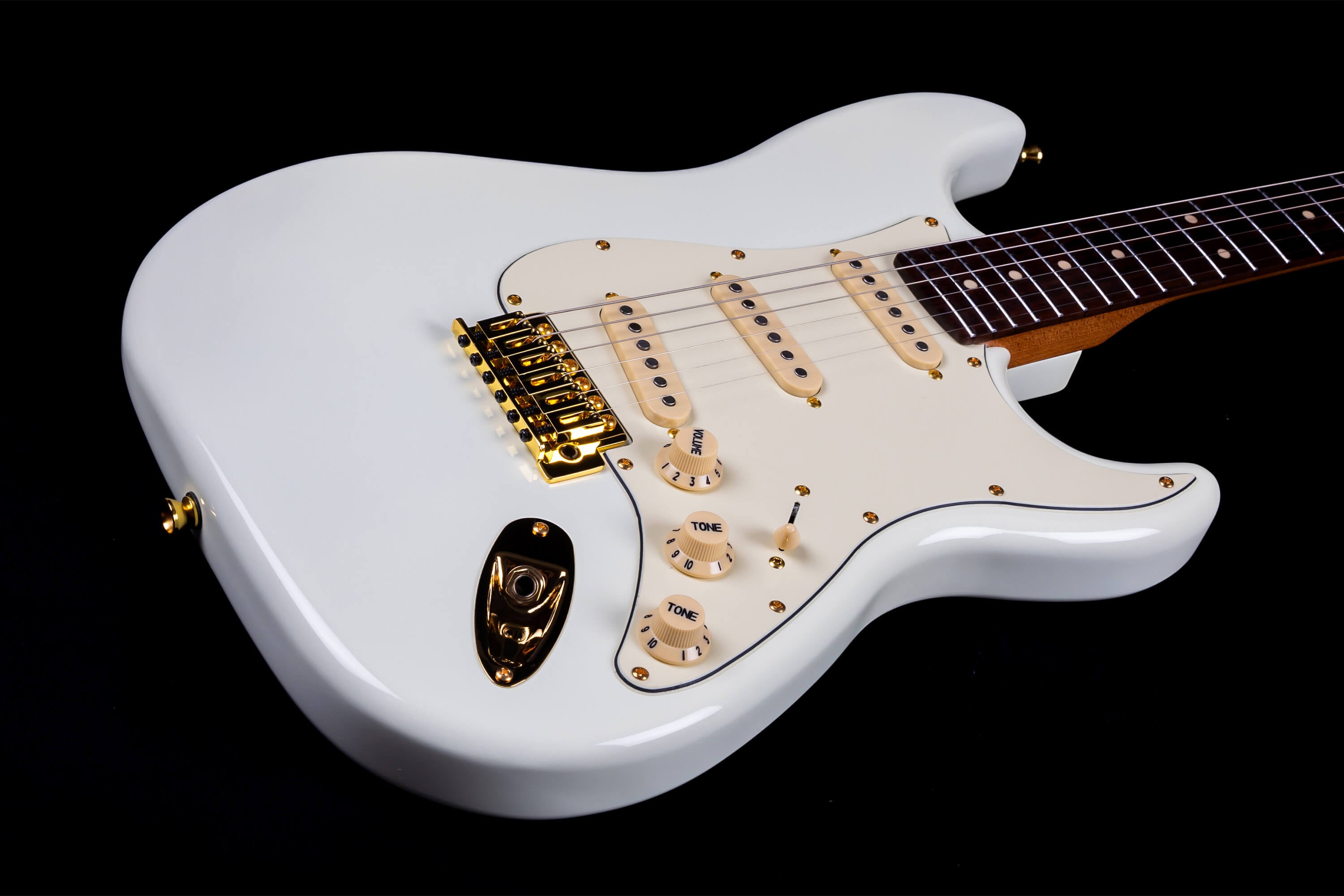 White electric guitar with gold hardware, cream pickups, cream knobs, and a dark fretboard against a black background.