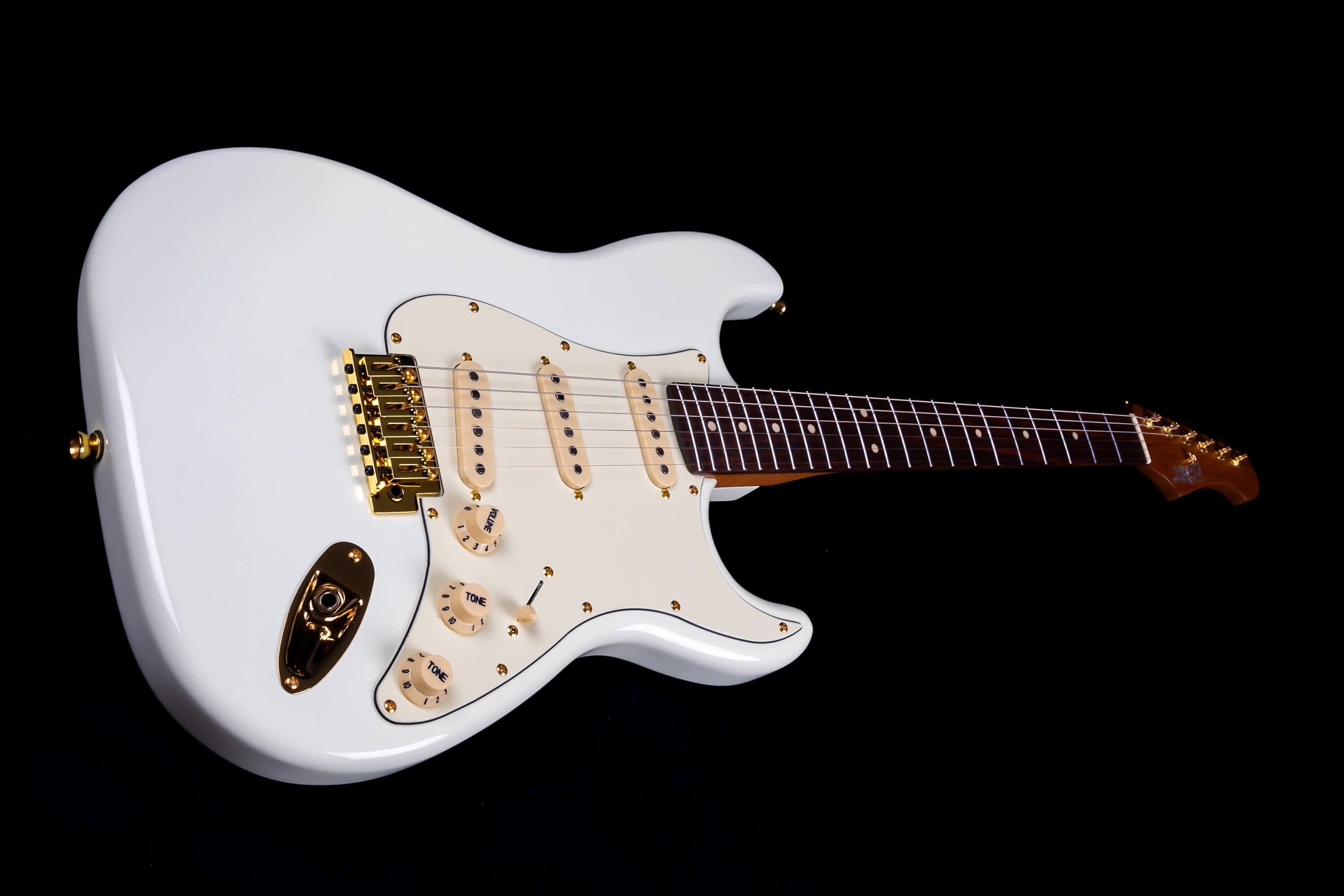 White electric guitar with gold hardware, three single-coil pickups, cream knobs, and a dark brown fretboard on a light wood neck.