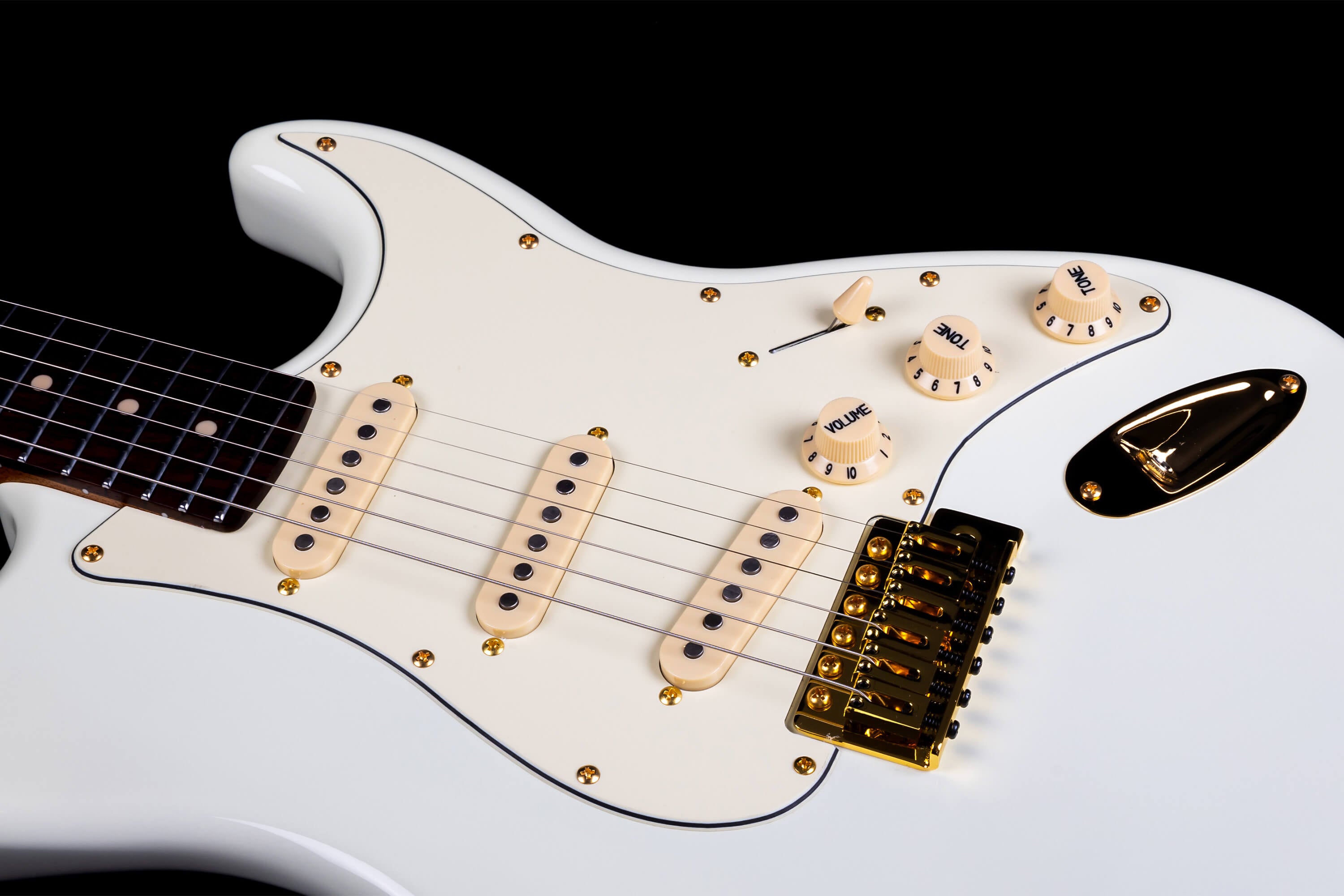 White electric guitar with gold hardware, cream pickup covers and knobs, and a rosewood fretboard partially visible at the left edge.