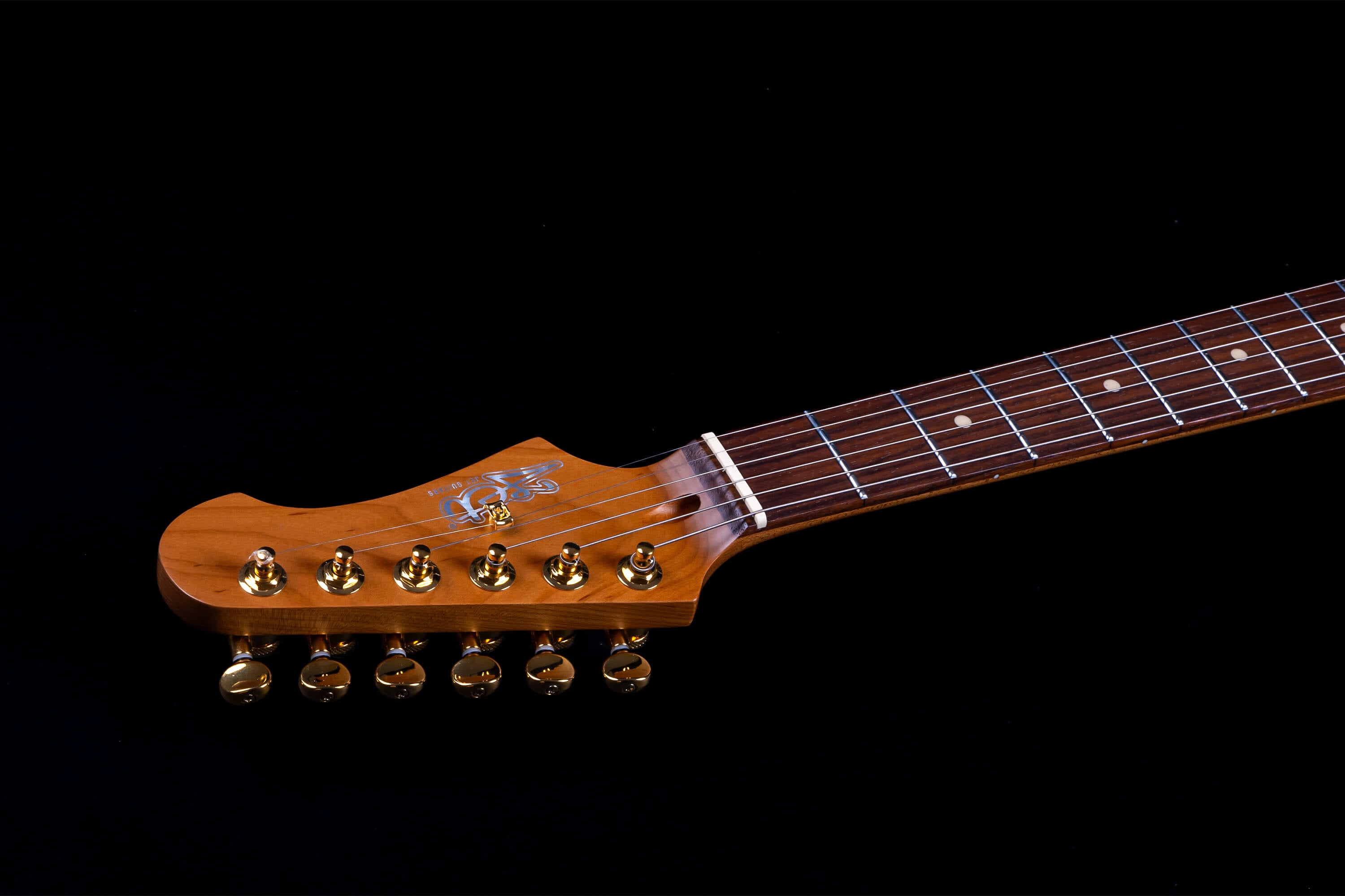 Jet Guitars headstock with gold tuning pegs, brown wood finish, silver logo, and part of a rosewood fretboard with dot inlays.