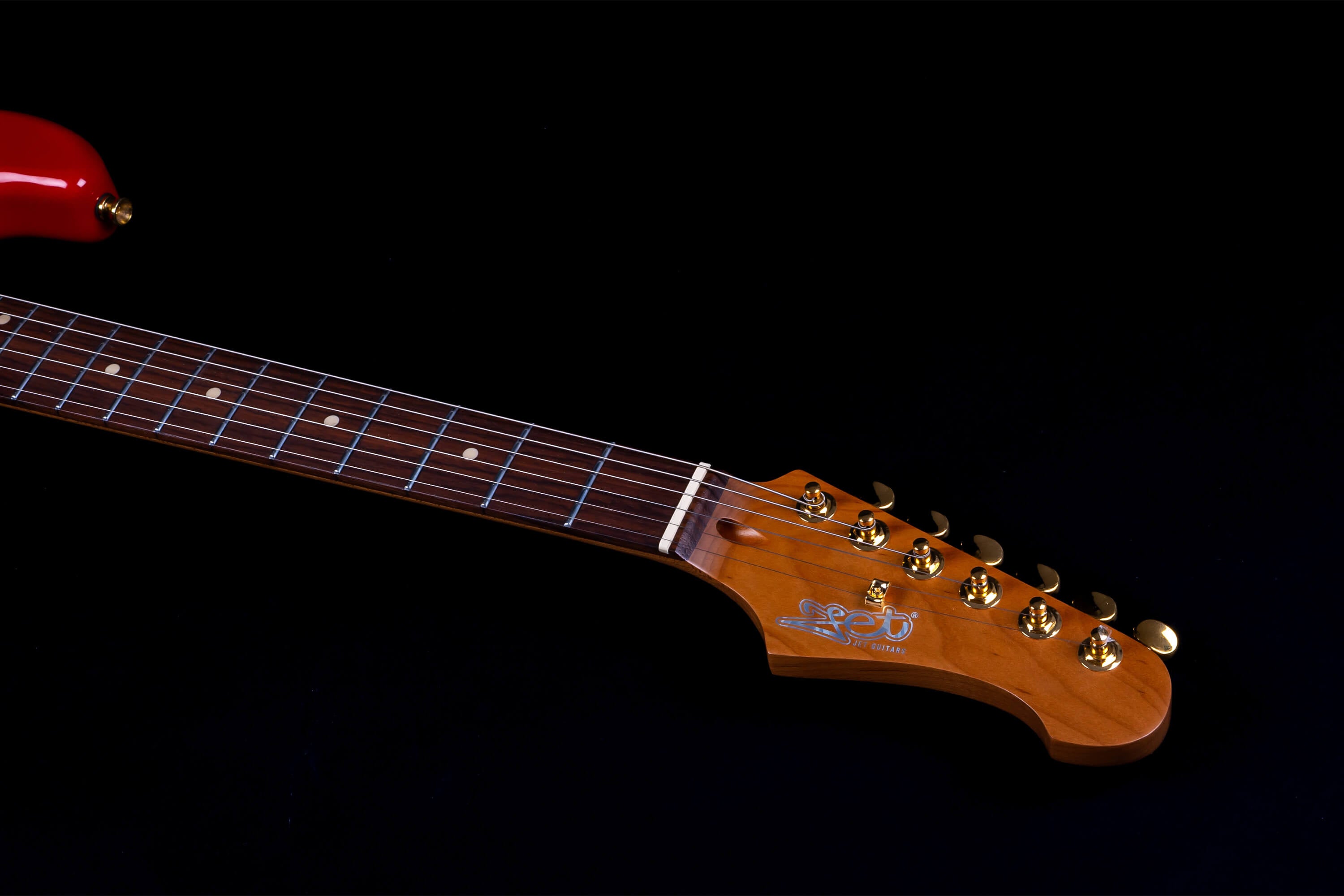 Jet Guitars electric guitar with a glossy red body, rosewood fretboard, and golden tuning pegs on a wooden headstock.