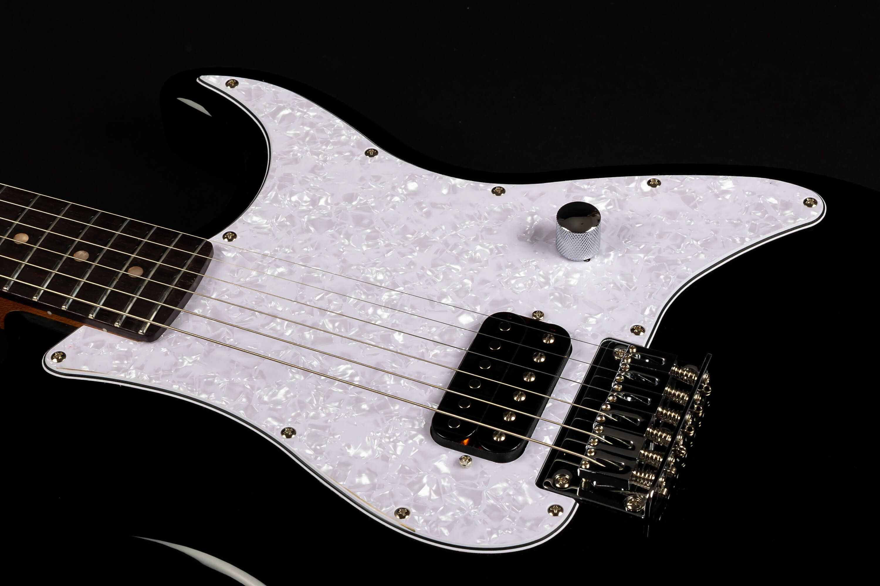 Electric guitar with a pearlescent white pickguard, single black pickup, chrome control knob, and six strings over a glossy black body.