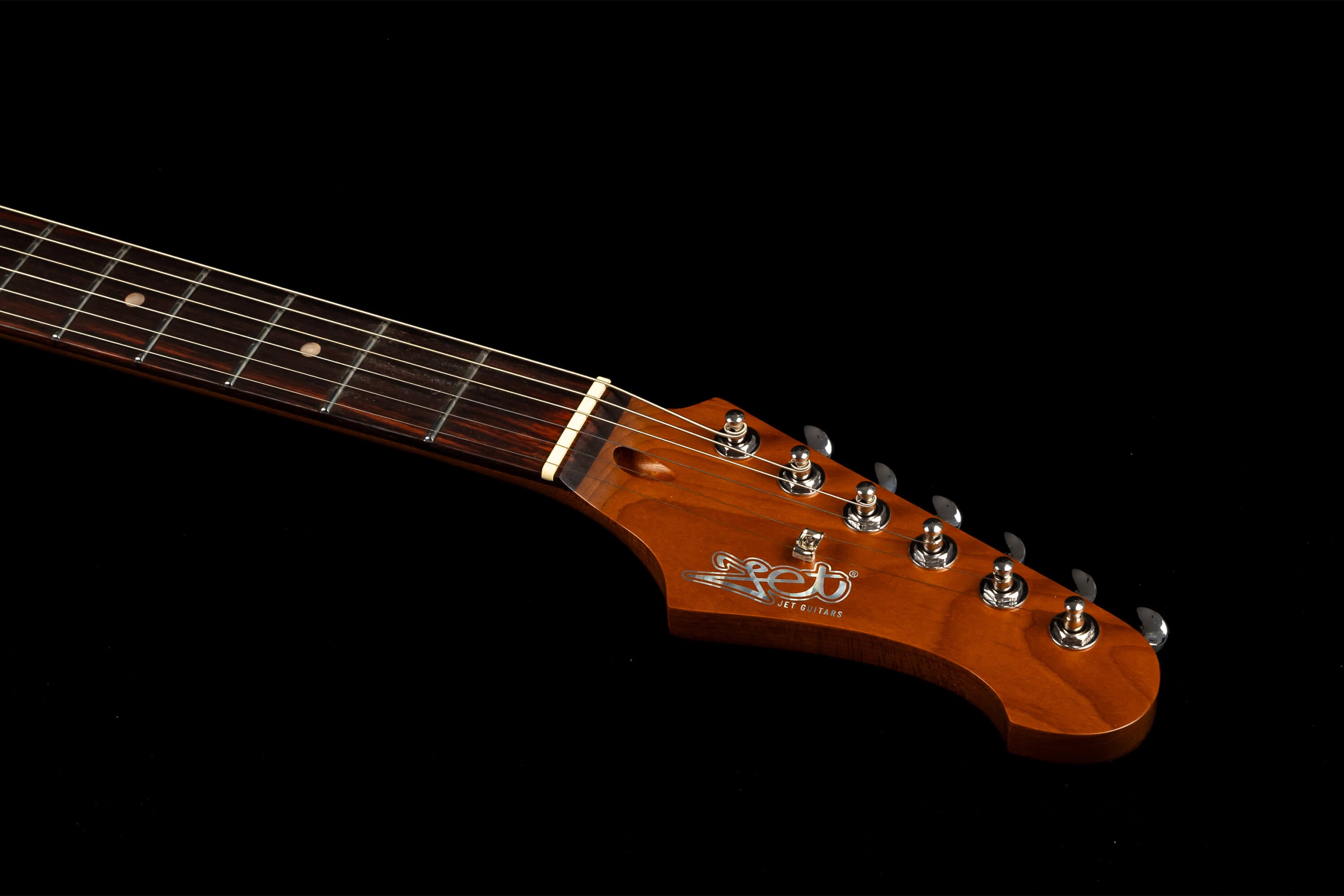 Six-string electric guitar neck and headstock with "Jet Guitars" logo, dark fretboard, white inlays, and chrome tuning pegs against a black background.