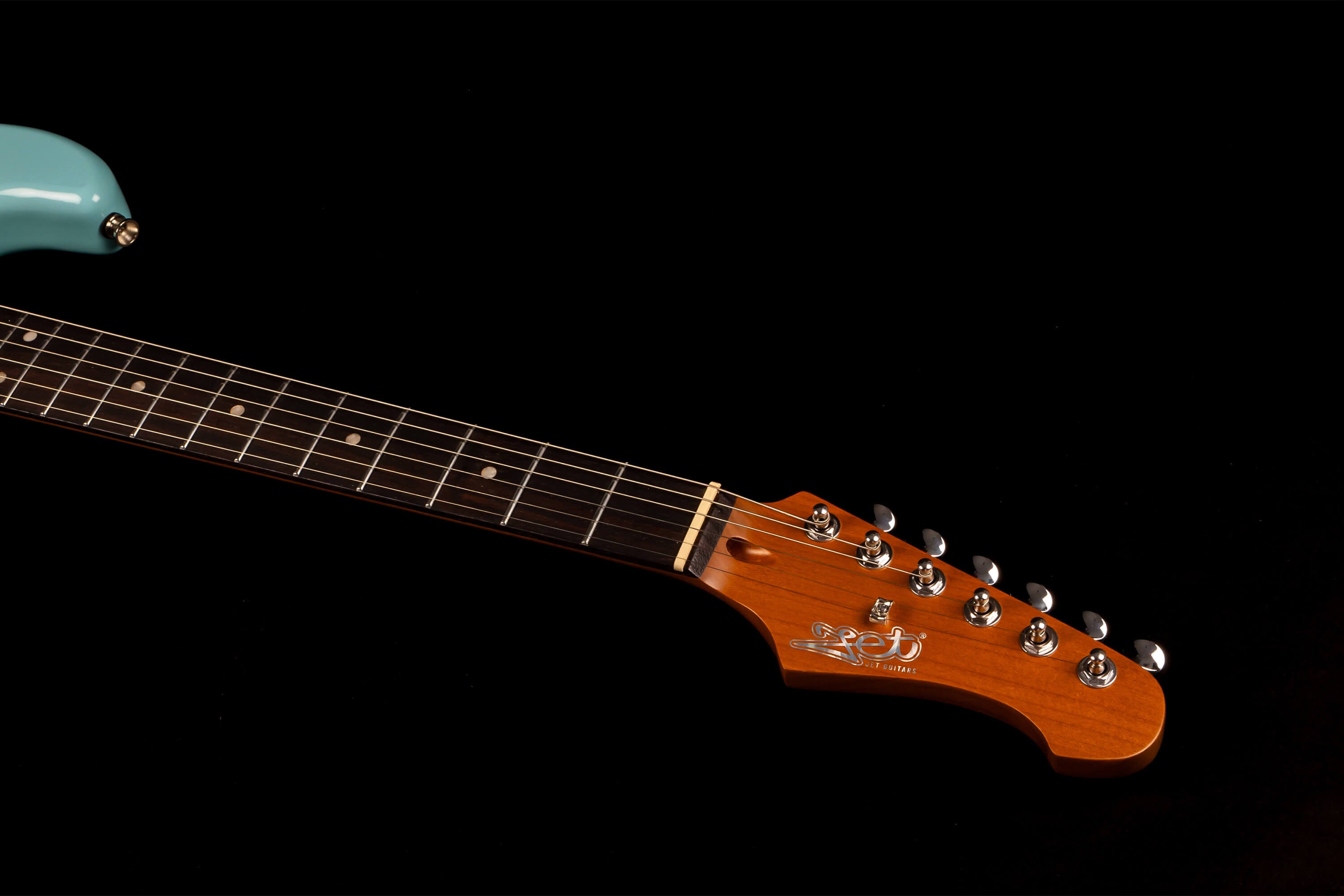 A light blue electric guitar shows its brown neck and headstock with six tuning pegs, silver frets, and white dot inlays on a dark background.