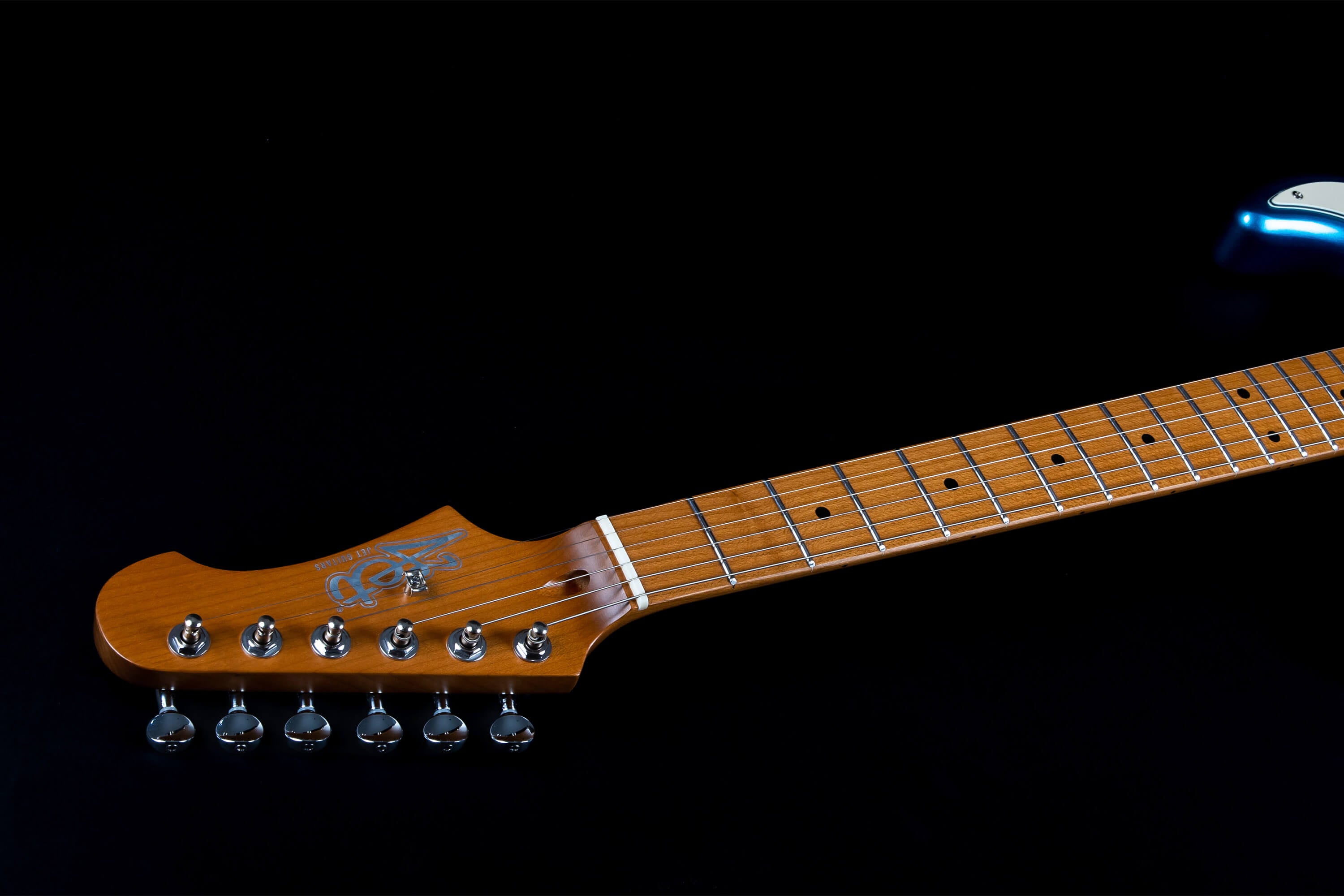Light brown electric guitar neck and headstock with six tuning pegs and silver logo, shown against a black background.