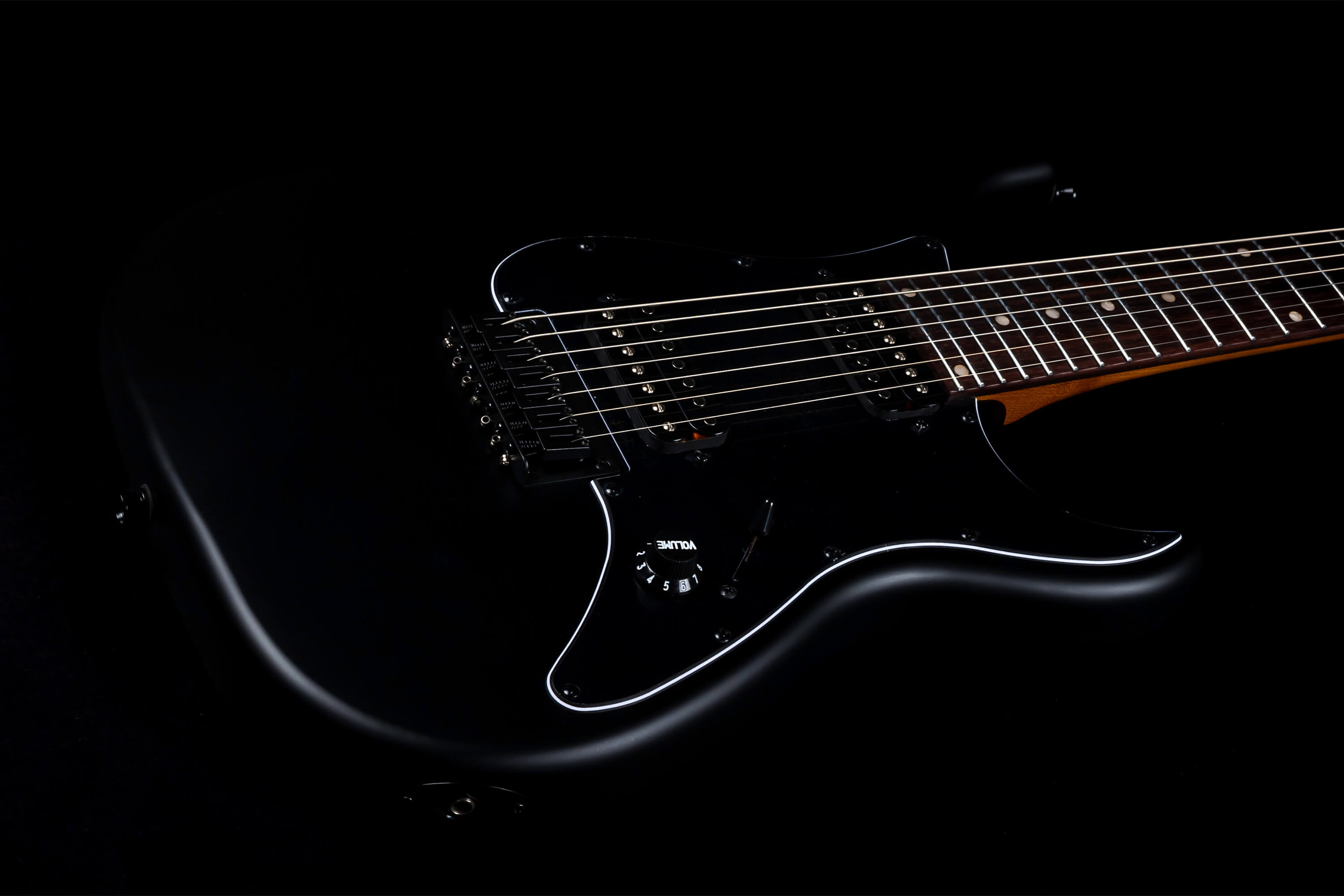 Matte black electric guitar with six strings, black pickups, a volume knob, and a dark fretboard with white dot inlays.