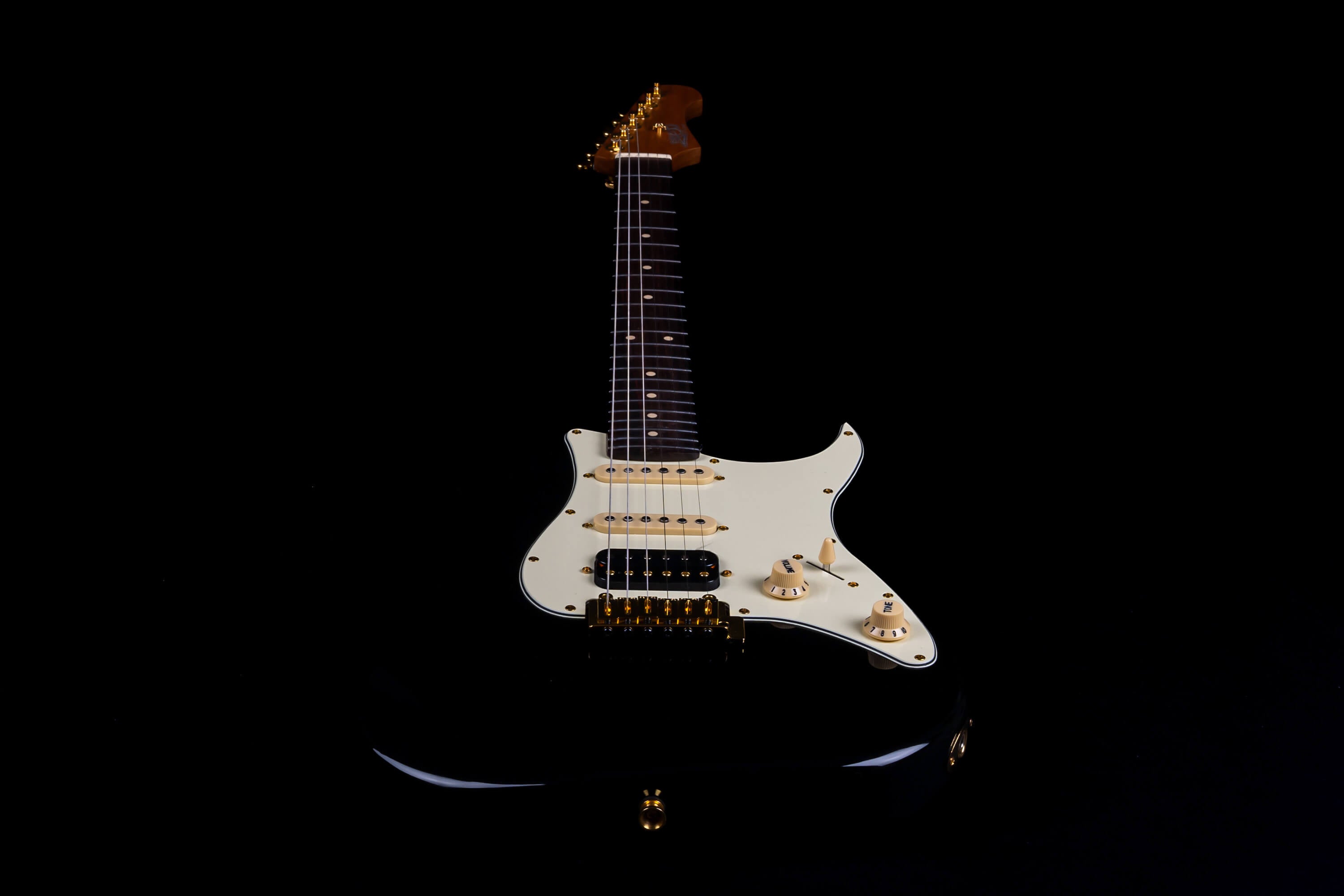 Black Jet electric guitar with cream pickguard, three single-coil pickups, gold hardware, and light-colored control knobs against a black background.