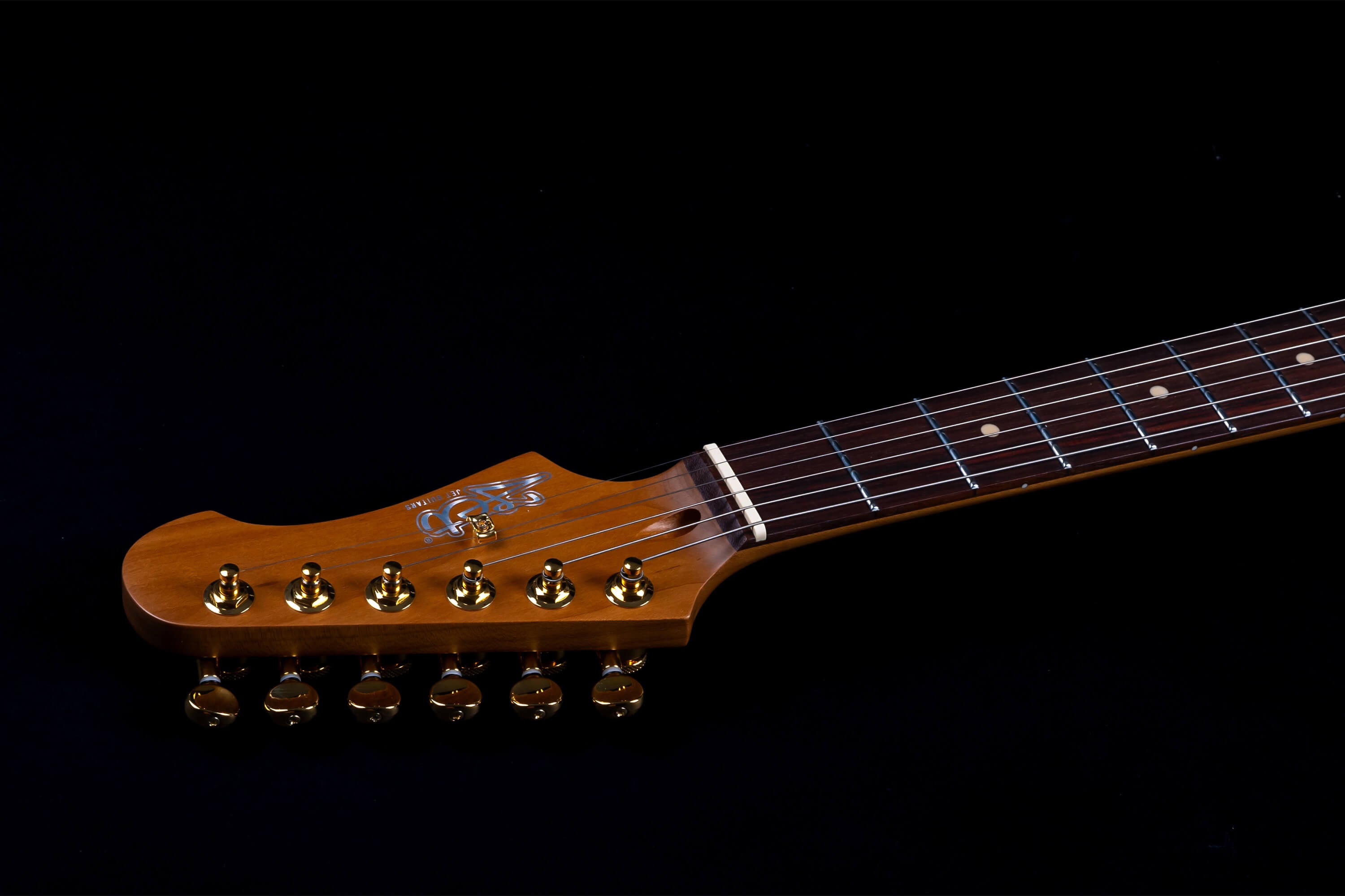 Jet Guitar headstock with gold tuning pegs, brown wood finish, and part of the fretboard with white dot inlays on a black background.