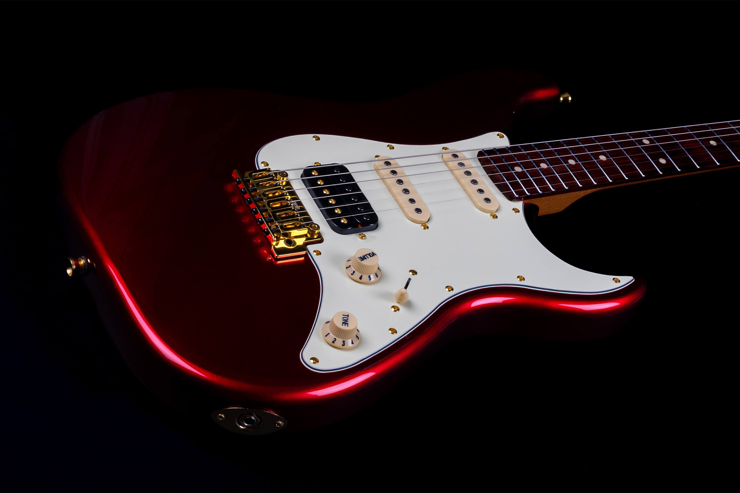 Red electric guitar with a white pickguard, gold hardware, three pickups, and a rosewood fretboard.
