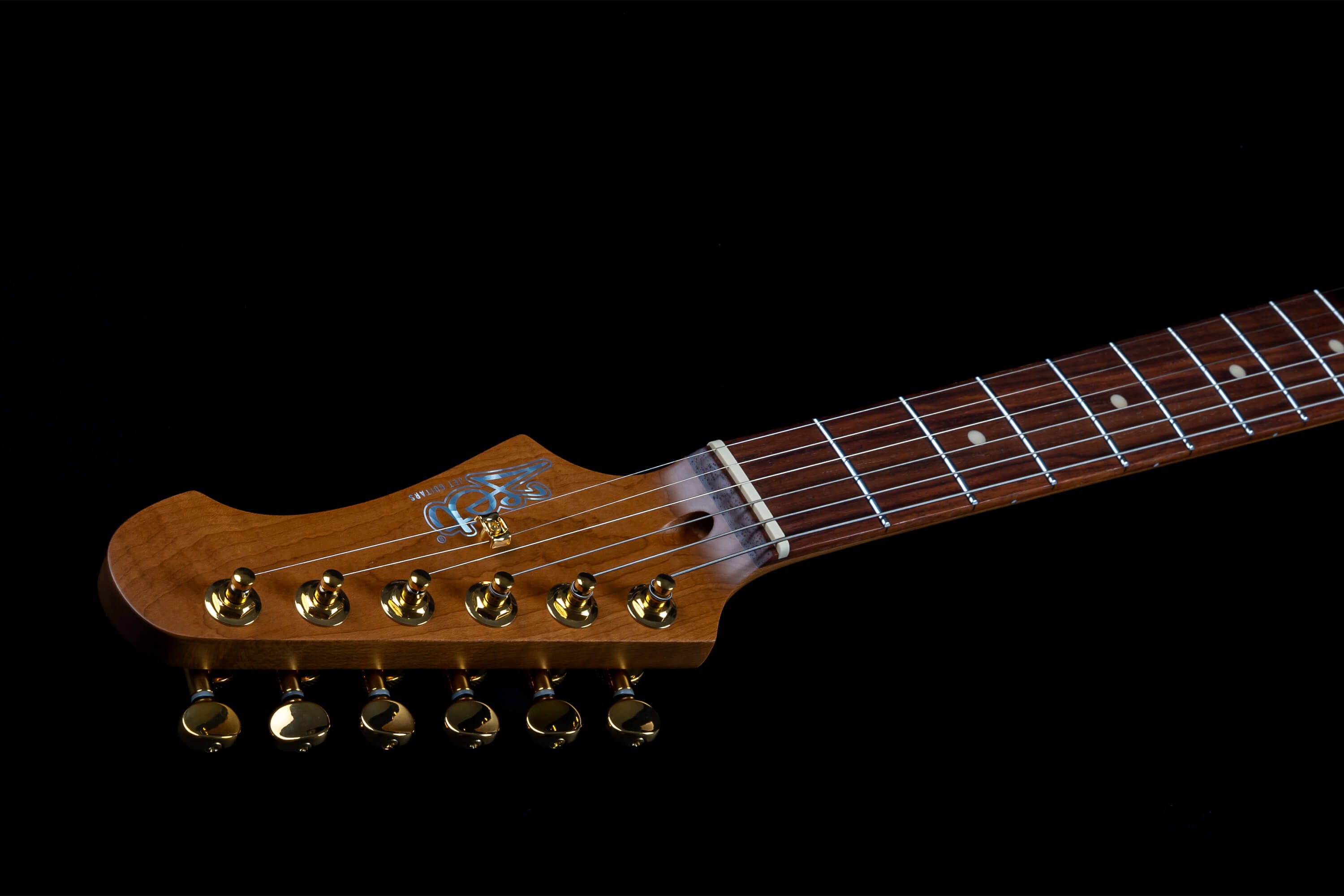 Electric guitar neck and headstock with six gold tuning pegs, dark wood fretboard, and circular fret markers on a black background.