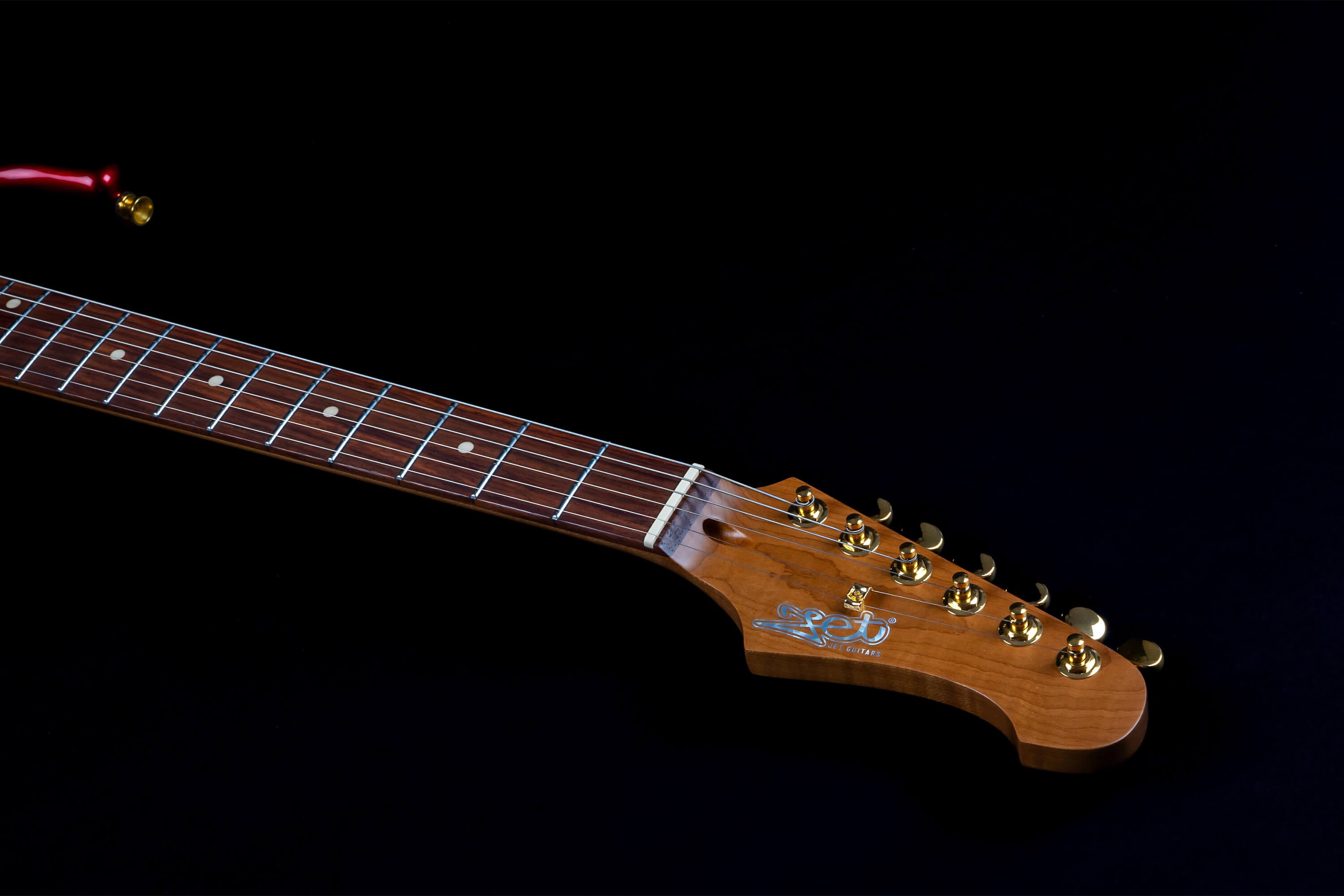 Electric guitar neck and headstock with six gold tuning pegs, rosewood fretboard, and white position markers on a black background.