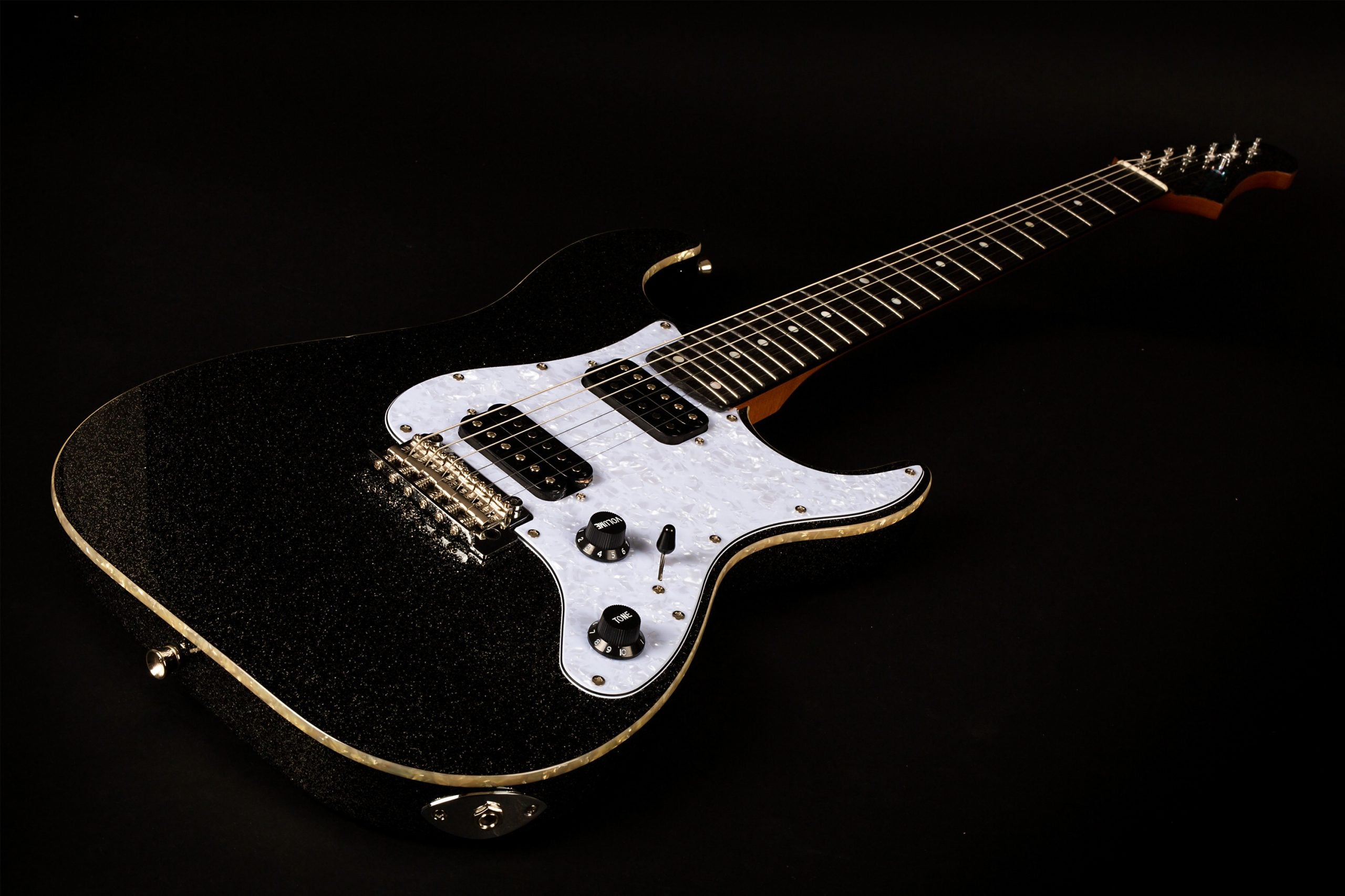 Black electric guitar with a white pearloid pickguard, two humbucker pickups, chrome bridge, and black control knobs, shown on a dark background.