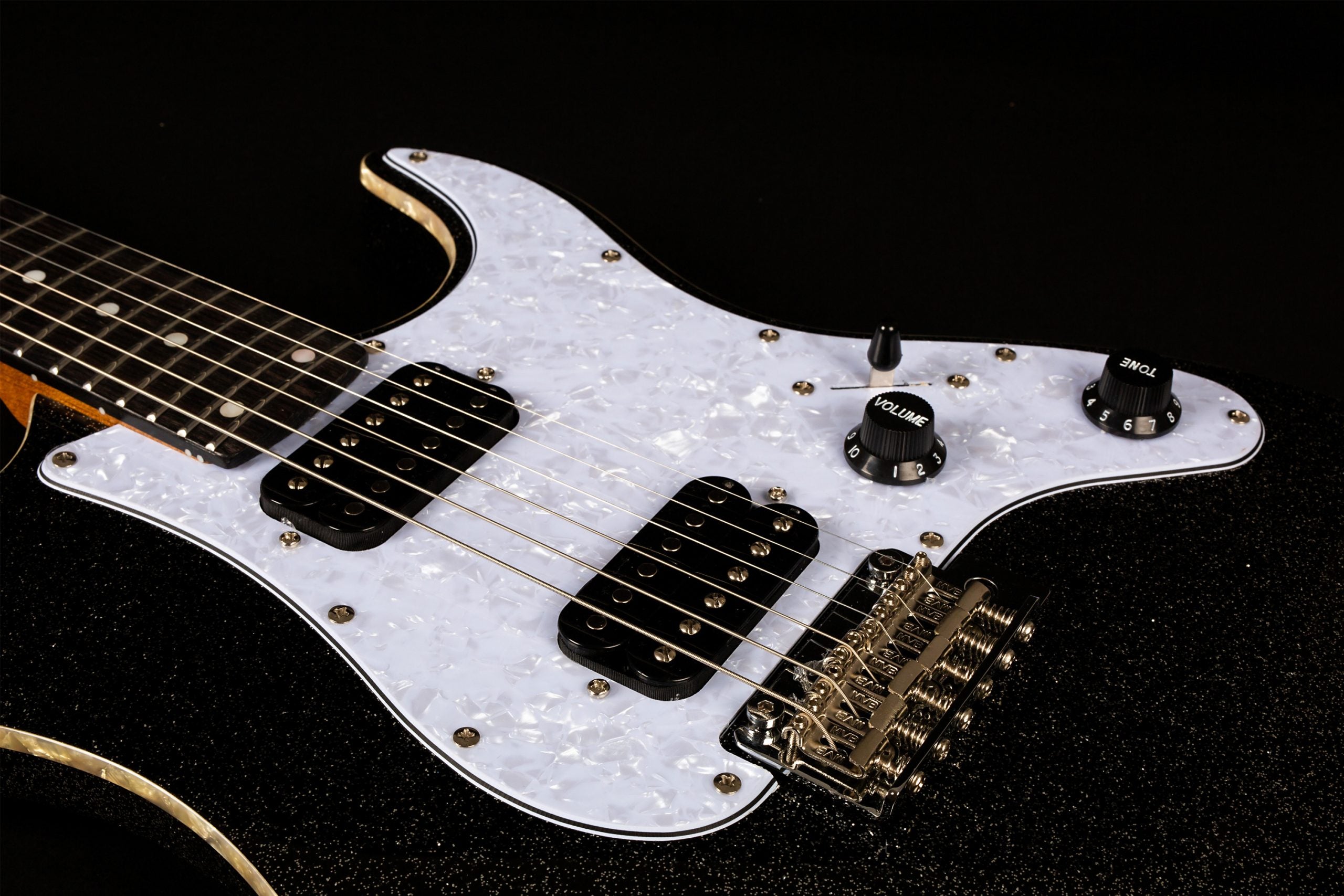 Electric guitar with a pearly white pickguard, black body, three pickups, two black knobs labeled volume and tone, and gold hardware.