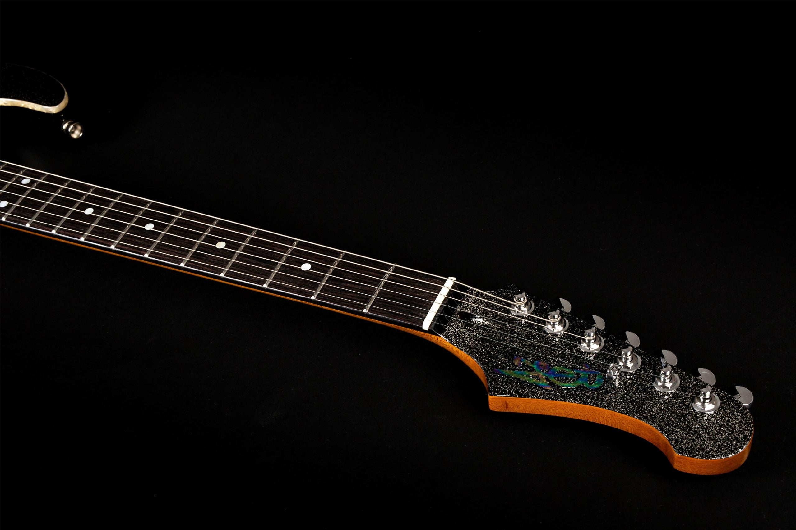 Electric guitar neck and headstock with six tuning pegs, black sparkly headplate, dot inlays on the fretboard, and a decorative colorful inlay.
