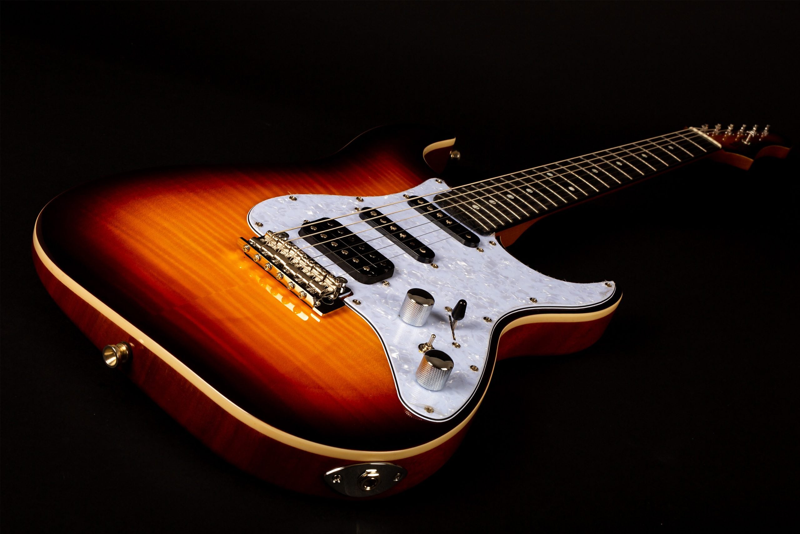 Sunburst electric guitar with a white pearloid pickguard, three pickups, two control knobs, and a five-way switch, lying on a black surface.